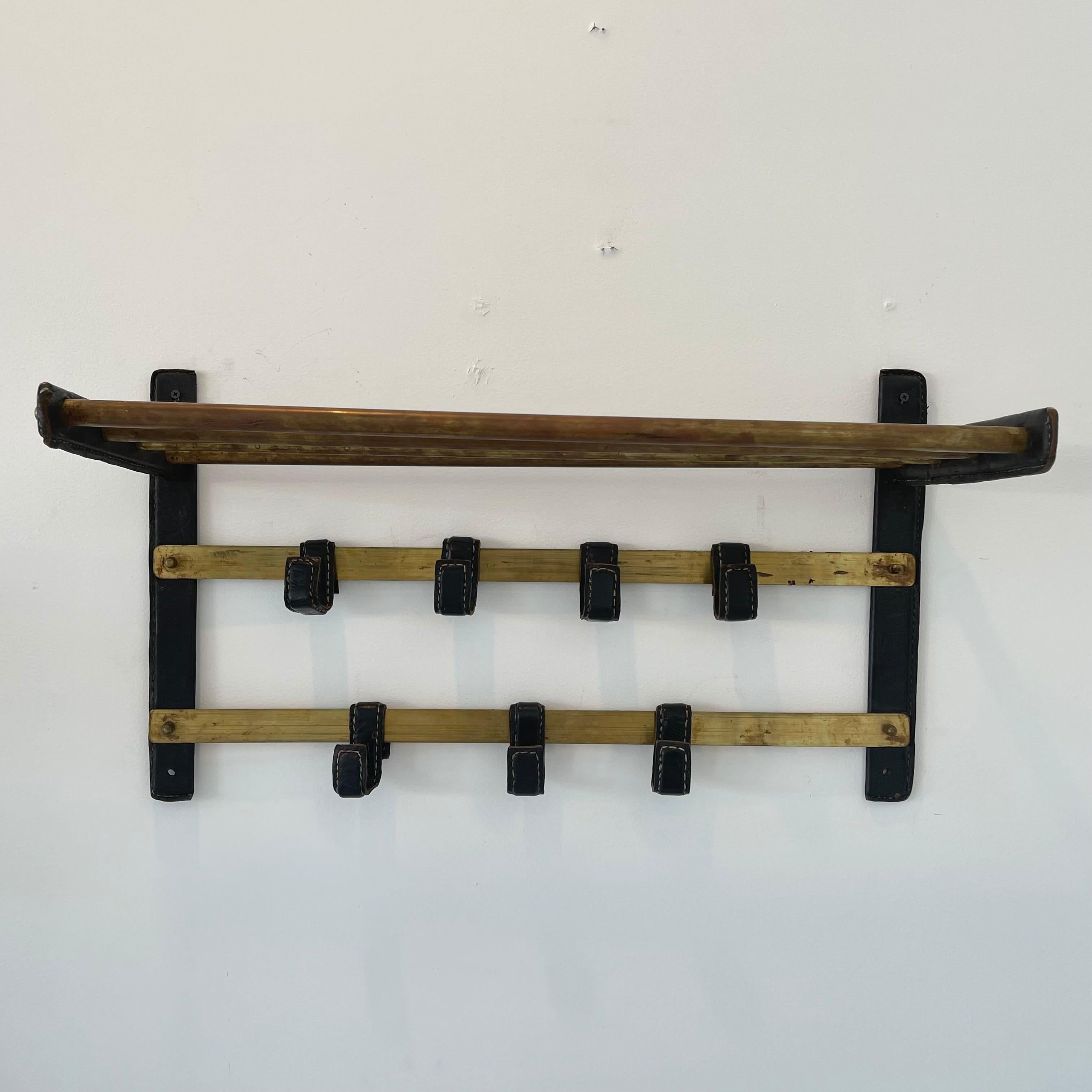 Stunning Jacques Adnet leather and brass wall rack with 7 moveable leather hooks. Right and left wall brackets wrapped in leather. Horizontal brackets also wrapped in leather. 4 heavy duty brass cross bars create a shelf on top. Extremely practical