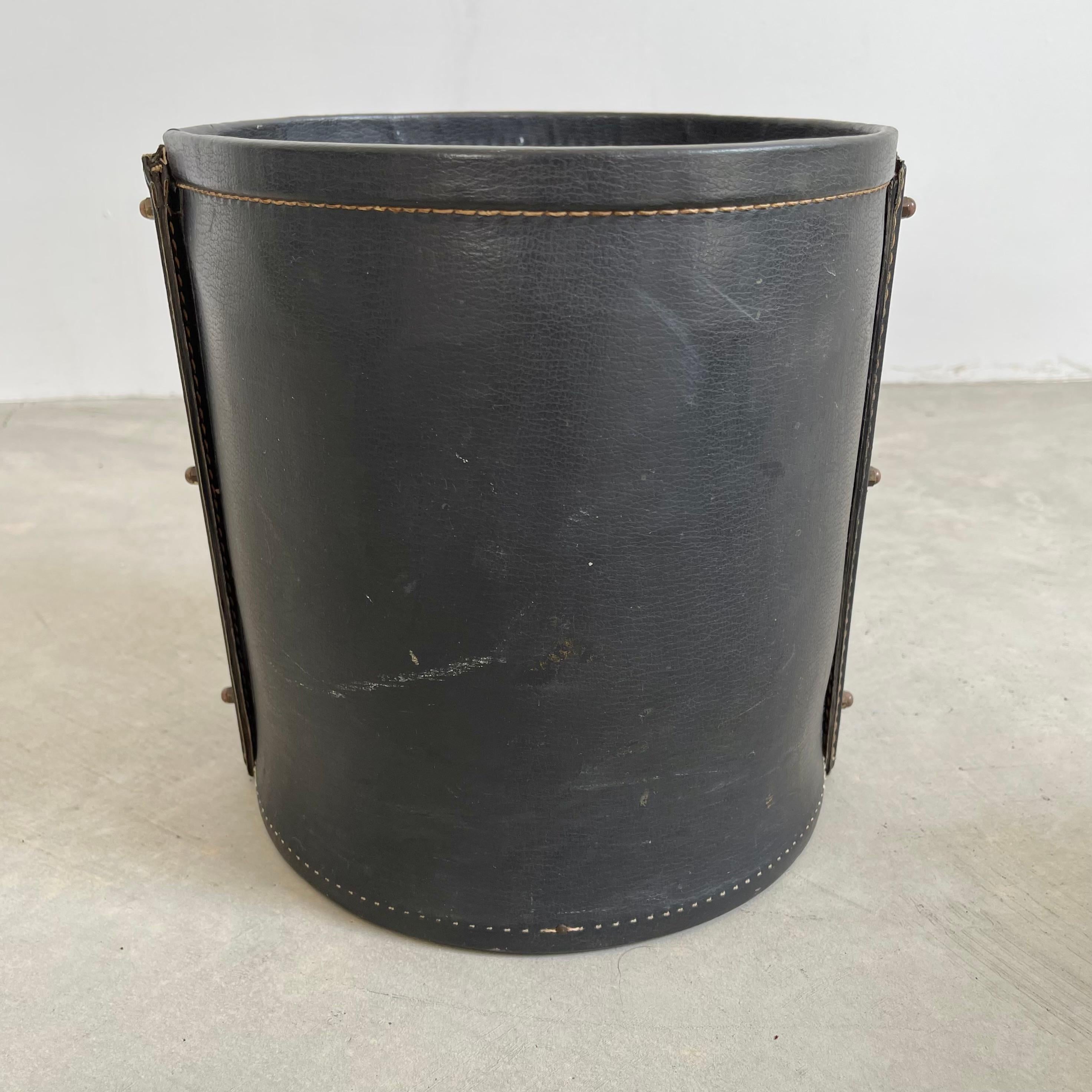 Handsome leather and brass waste basket by French designer Jacques Adnet. Completely wrapped in leather with brass hardware. Good vintage condition and patina to leather and brass. Wood bottom. Very sturdy. Great lines. Collectible piece of Adnet