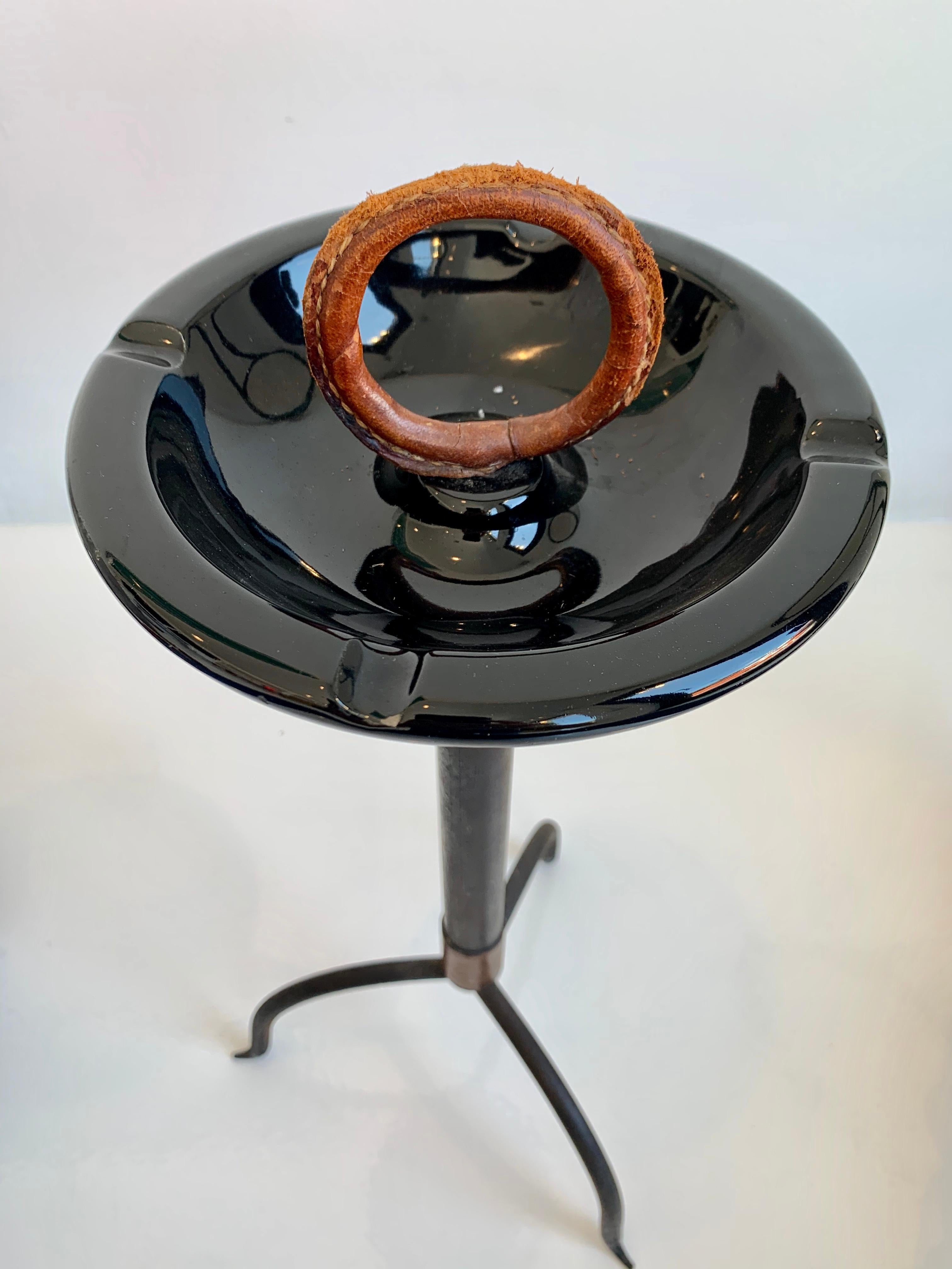 Stunning leather and iron catchall / ashtray by Jacques Adnet. Iron frame on three slender legs. Ceramic dish with saddle leather, circular pull on top. Saddle leather wrap at bottom of iron frame as well. Signature Adnet contrast stitching. Great
