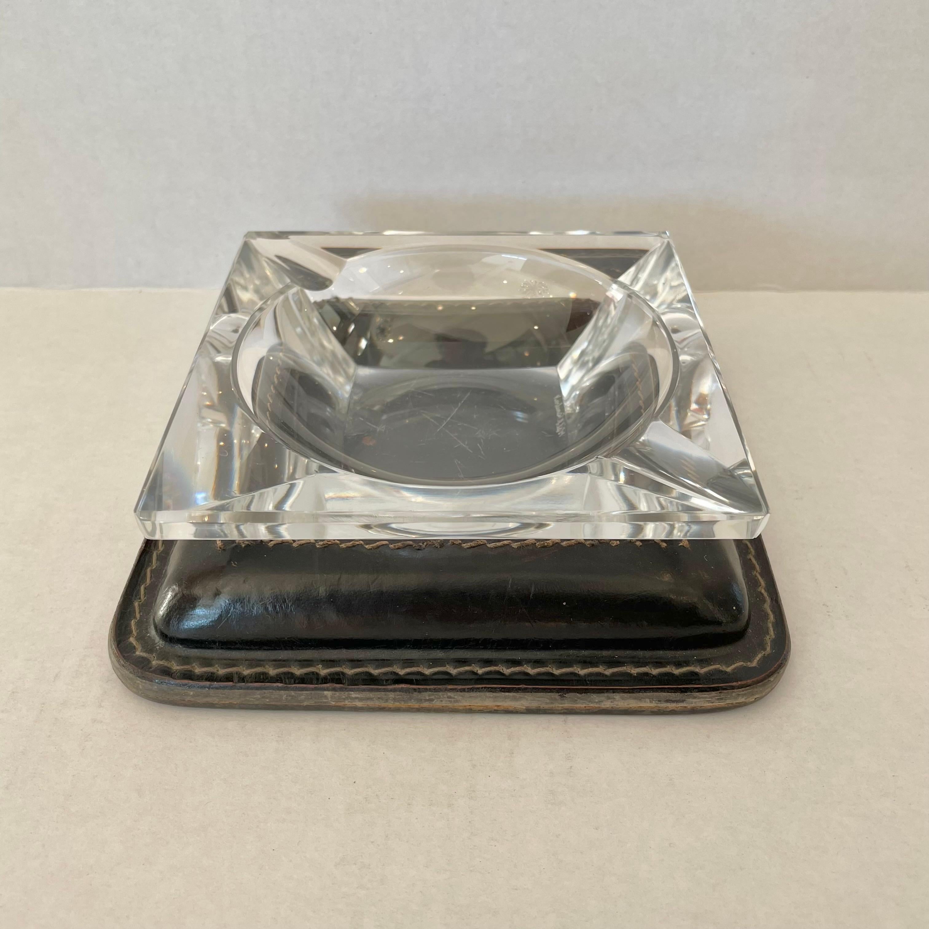 Classic leather and glass catchall / ashtray by French designer Jacques Adnet. Rich black leather base with signature Adnet contrast stitching and a circular inset cutout. Crystal glass with circular base sits nicely inside with two cigarette