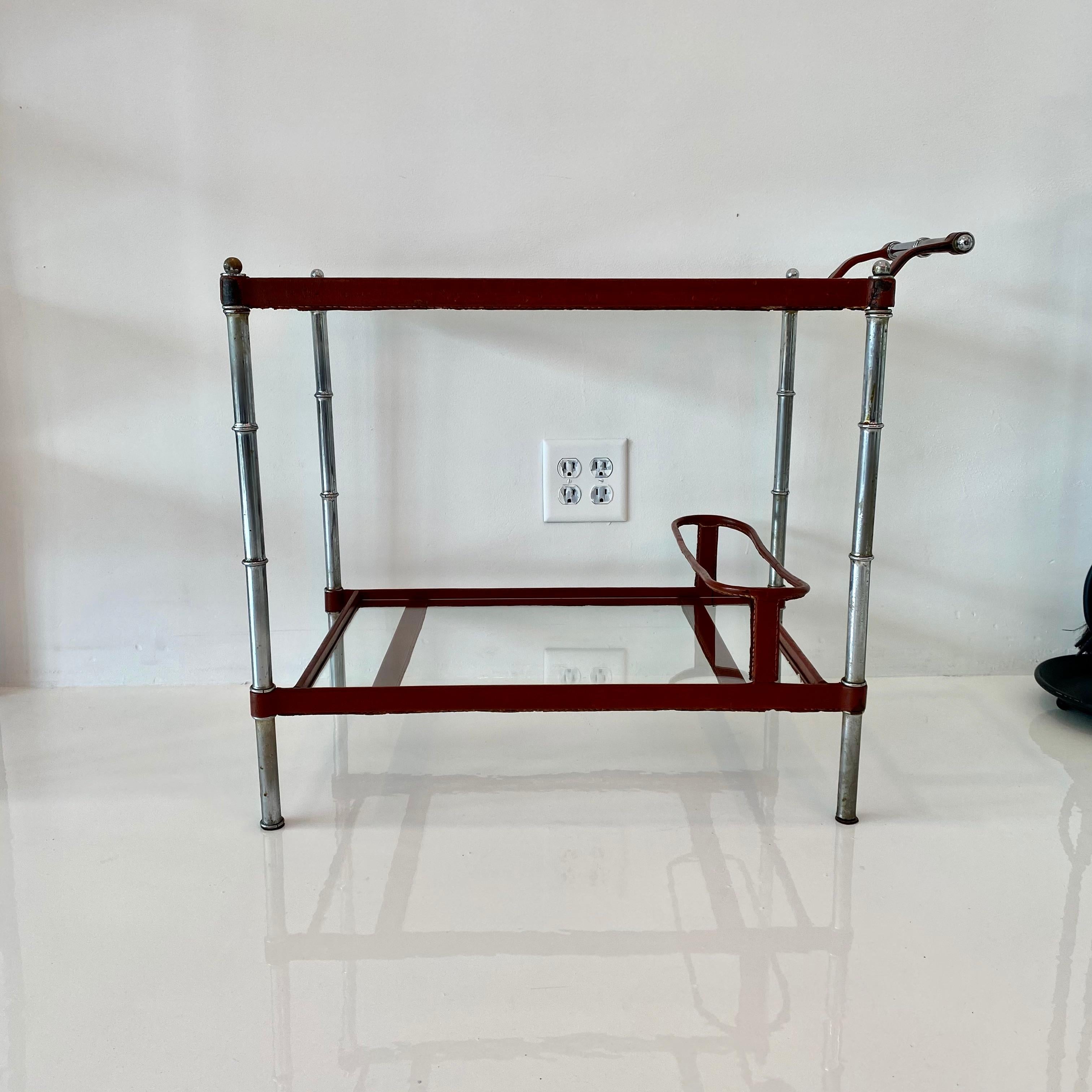 Handsome bar cart by French designer Jacques Adnet. Leather wrapped frame with two glass shelves. Offered with or without casters. Leather wrapped bottle holder on bottom shelf. Deep burgundy leather with Classic Adnet contrast stitching throughout.