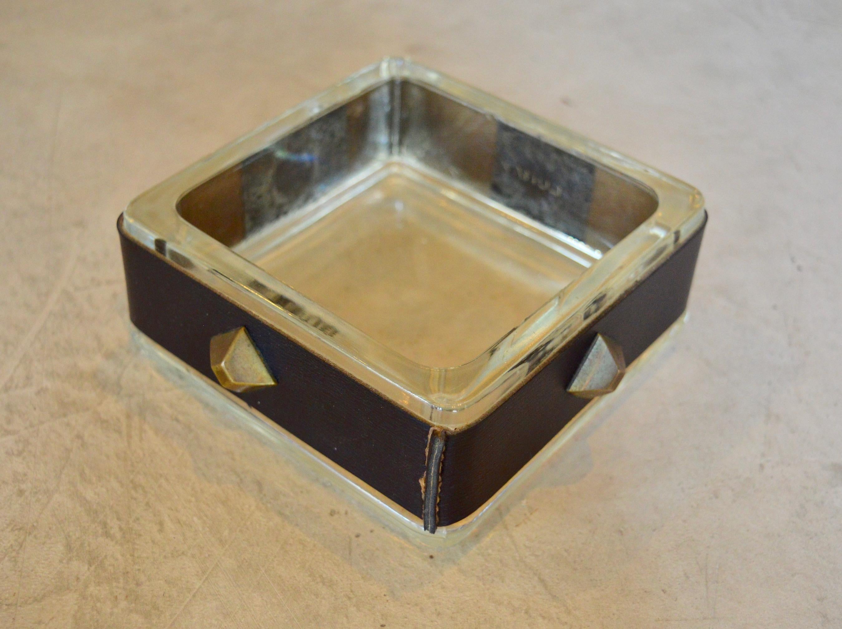 Handsome black leather and glass ashtray / catchall by French designer Jacques Adnet. Signature Adnet contrast stitching throughout. Brass stud details on all sides. Great desktop piece or catchall to put by the front door. Very good vintage