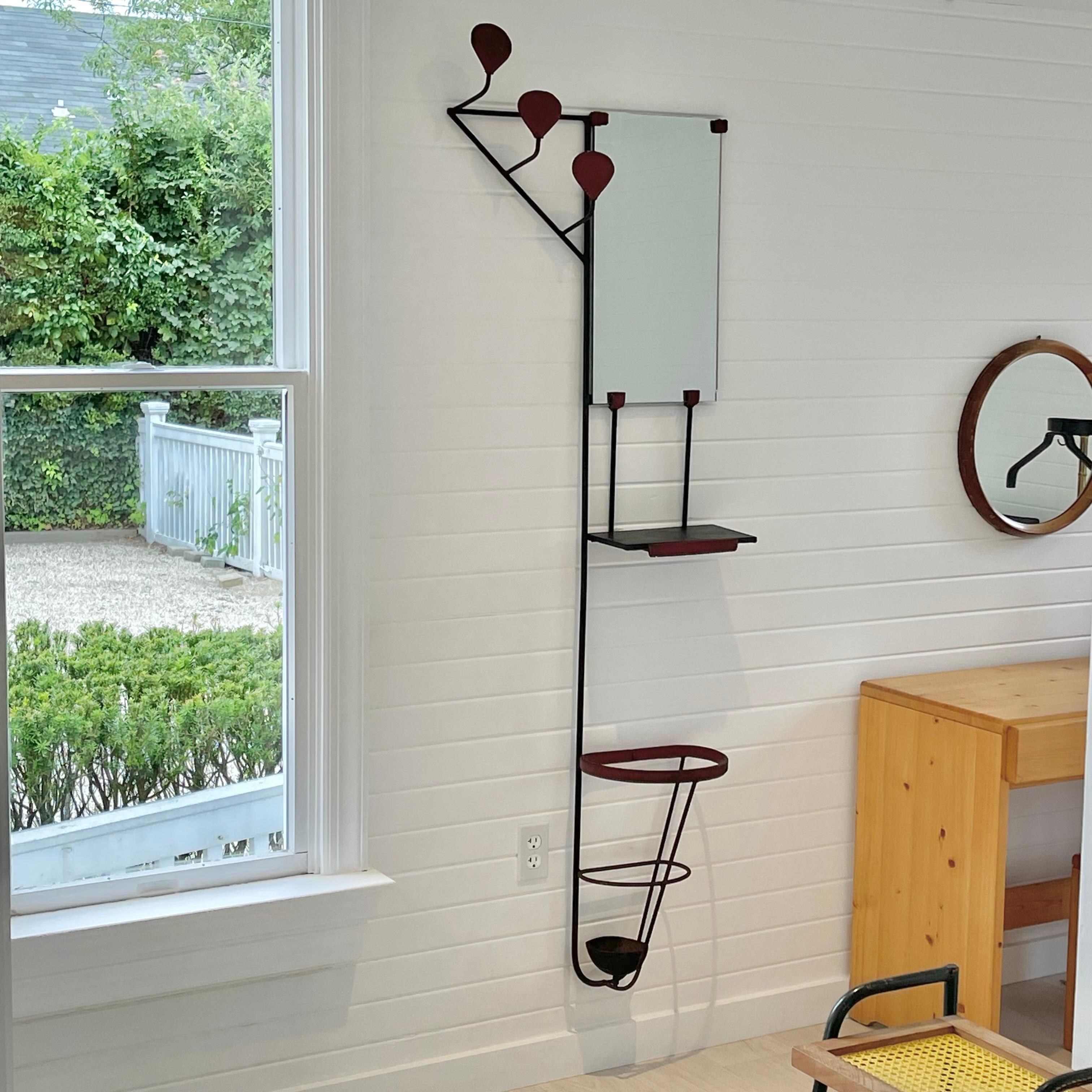 Stunning leather and iron wall rack by Jacques Adnet. Rack consists of three hooks descending from top left, a mirror and umbrella holder. A small shelf suspends from mirror, perfect for wallet, keys etc. Original water catcher at bottom of umbrella