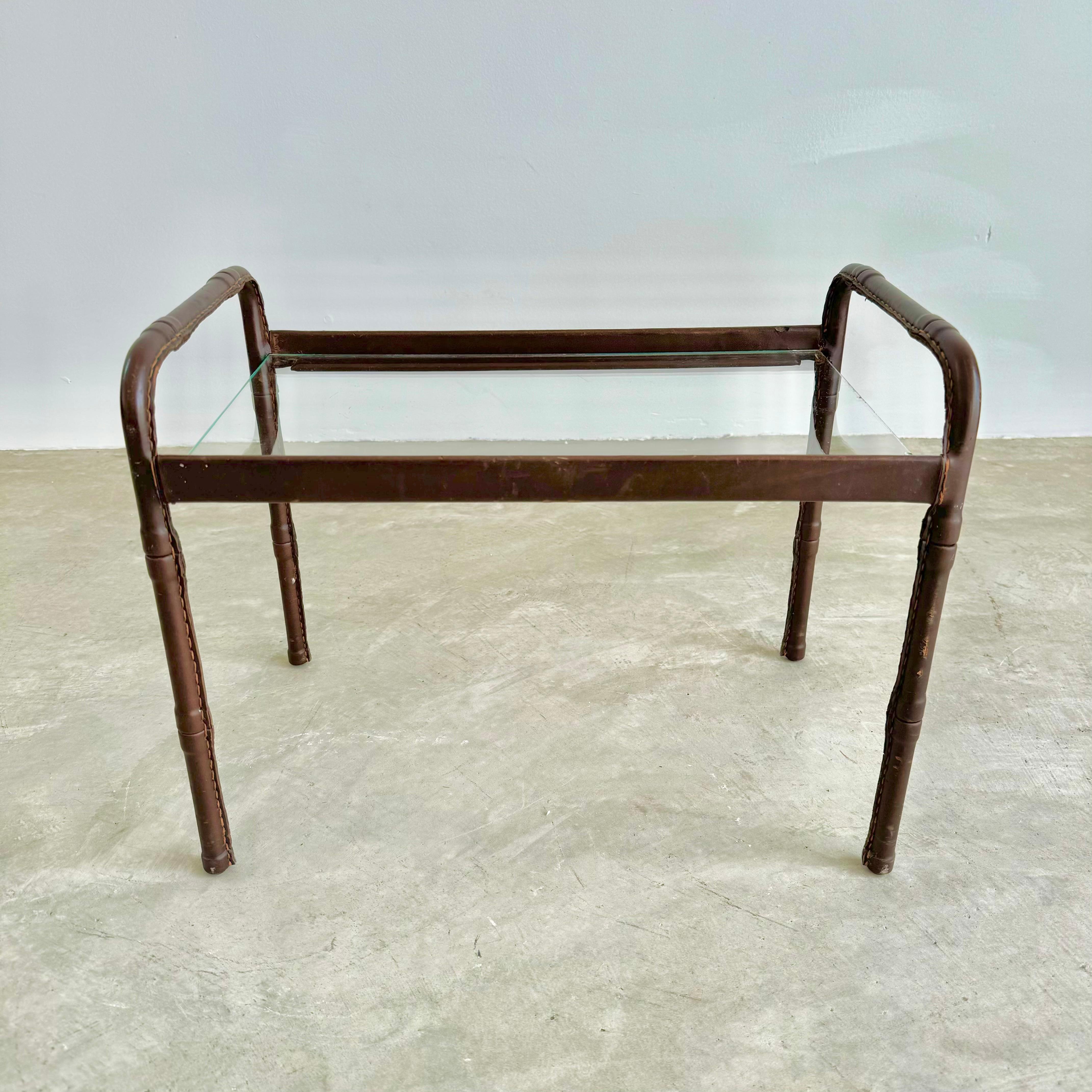 Superbe table d'appoint en cuir avec plateau en verre du designer français Jacques Adnet. Cadre en fer enveloppé d'un beau cuir brun. Les deux extrémités sont définies par deux arcs enveloppés de cuir qui forment les poignées du plateau et les pieds