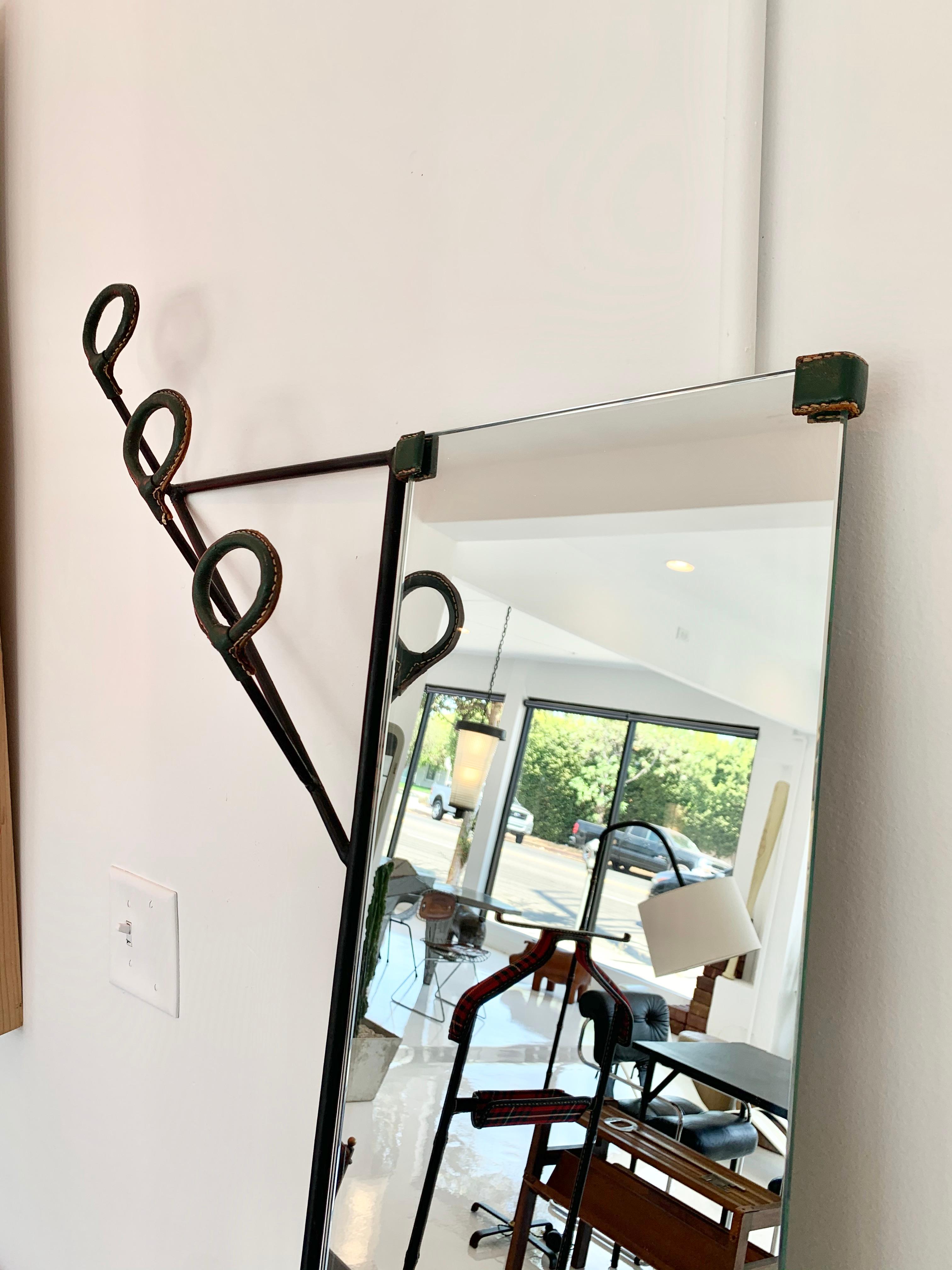 Stunning wall rack by Jacques Adnet. Rack consists of three hooks, a mirror and umbrella holder. Iron frame with dark green saddle leather with signature Adnet contrast stitching. Stunning piece of collectible Adnet. Extremely functional and rare.