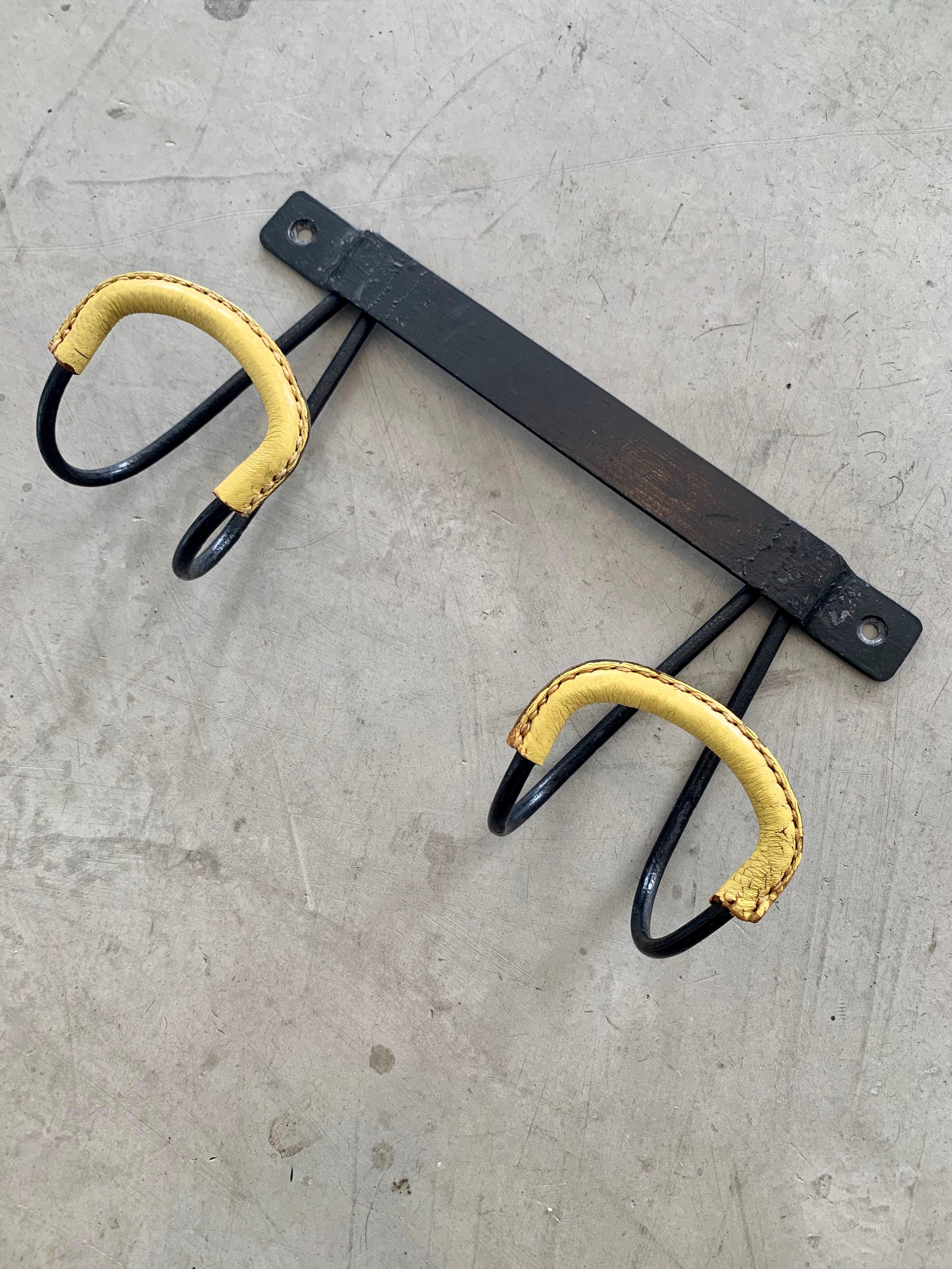 Handsome coat rack by Jacques Adnet. Iron frame with iron tongue hooks wrapped in yellow leather with signature Adnet contrast stitching. Great vintage condition.

  