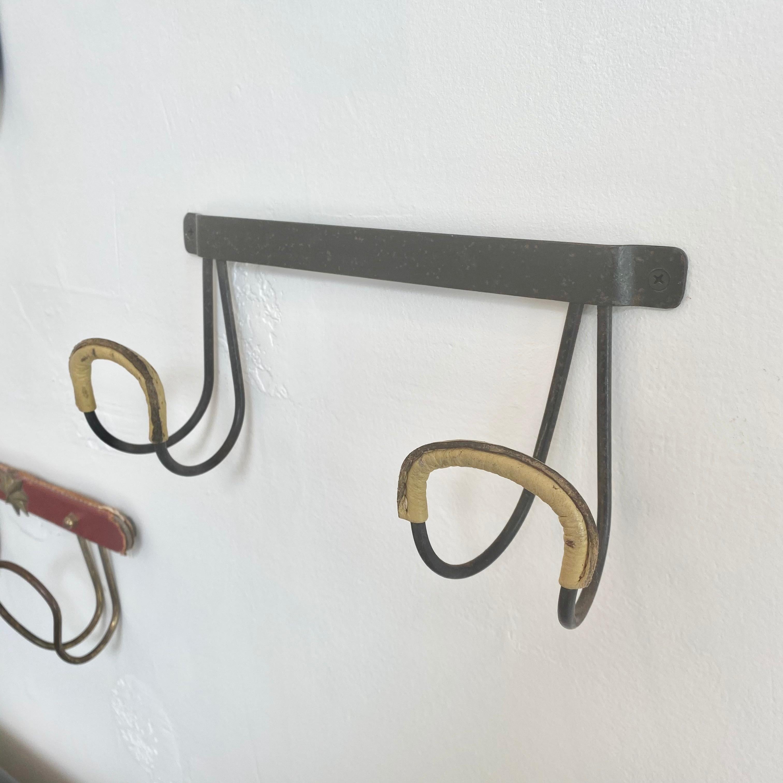 Handsome coat rack by Jacques Adnet. Iron frame with iron tongue hooks wrapped in yellow leather with signature Adnet contrast stitching. Great vintage condition.

  