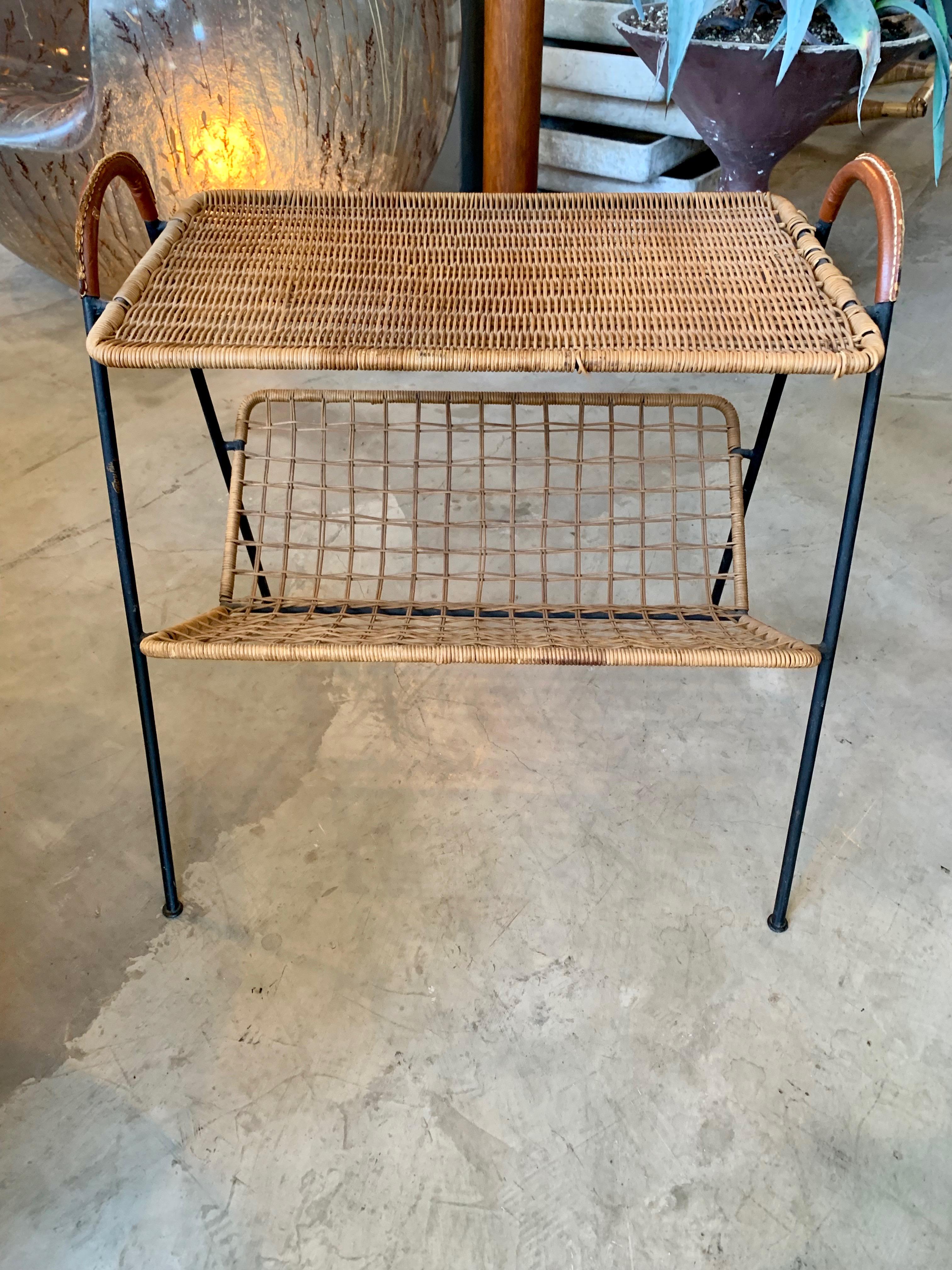 Stunning side table by Jacques Adnet. Iron frame with saddle leather wrapped handles and signature Adnet contrast stitching. Handwoven wicker tabletop with woven wicker slanted shelf underneath. Exceptional piece of collectible Adnet. Good original