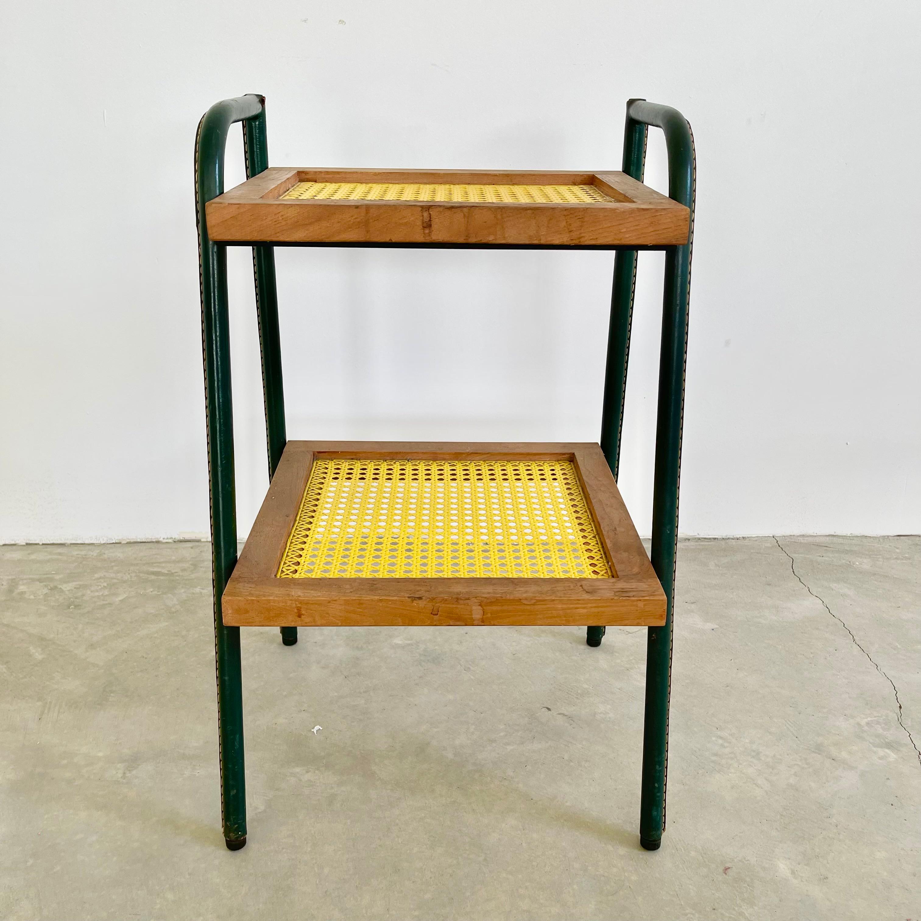 Stunning leather and wood side table by Jacques Adnet. Iron frame completely wrapped in green leather. Yellow table surfaces are made of plastic wicker woven to resemble caning. Signature Adnet contrast stitching. Iron ball feet. Great vintage
