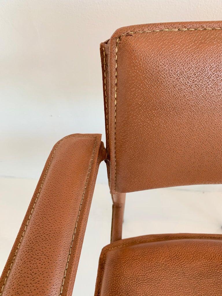 Rare fauteuil en cuir et en fer du designer français Jacques Adnet. La chaise est entièrement recouverte de cuir cousu à la main. Pieds plafonnés en laiton et détails de quincaillerie en laiton sur les dossiers des chaises. Le fond et le dossier de