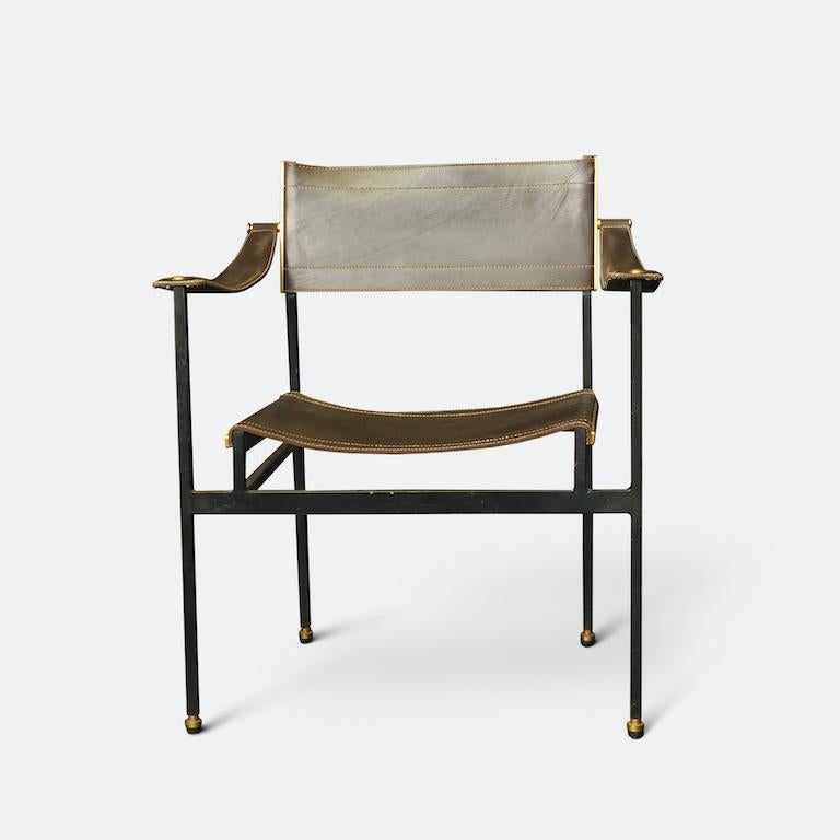 Un fauteuil rare de Jacques Adnet datant des années 1950. 
Construit sur un cadre angulaire en métal noir, l'assise, le dossier et les accoudoirs sont bordés de surpiqûres sellier, signature d'Adnet, en cuir blanc contrastant avec le cuir brun