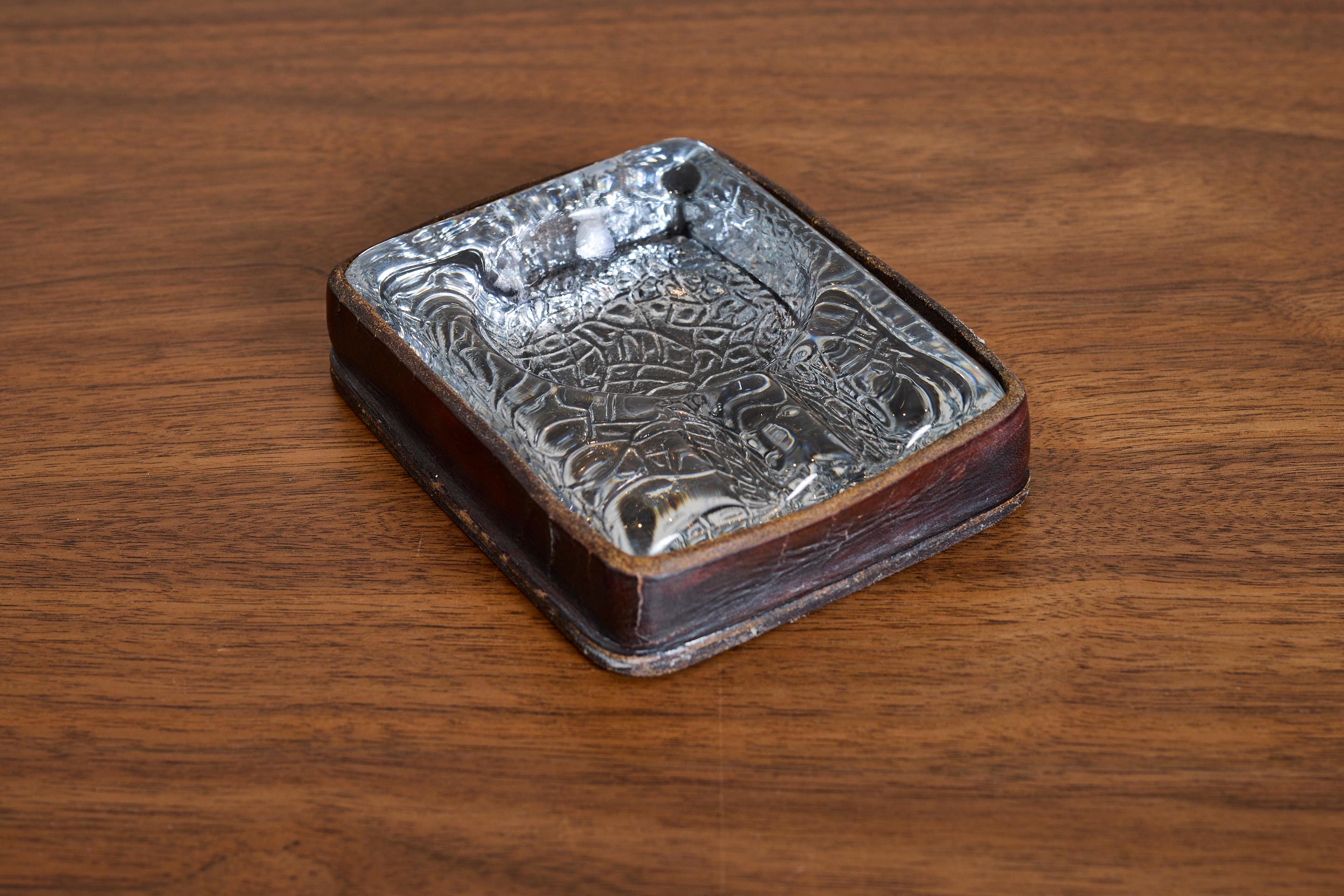 Handsome Jacques Adnet ashtray set in beautifully worn dark brown leather. 

Thick molded glass with crackle detailing

Incredible piece.

France 1940s.