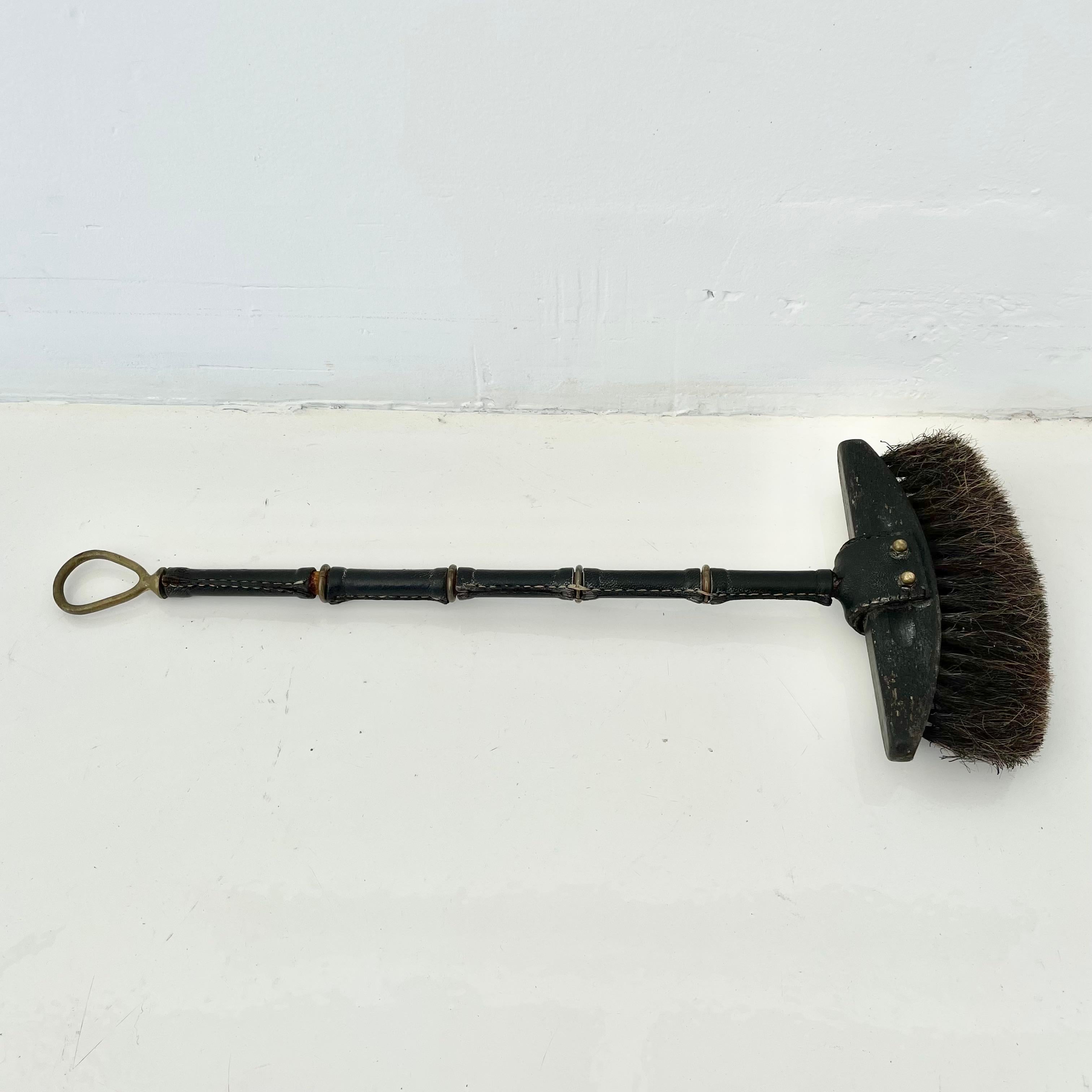 A very rare fireplace broom by Jacques Adnet. Classic Adnet style with the shaft fully wrapped in black leather spaced with brass rings and a brass loop on the end of the handle for hanging. The wooden head is attached with a leather crown and brass