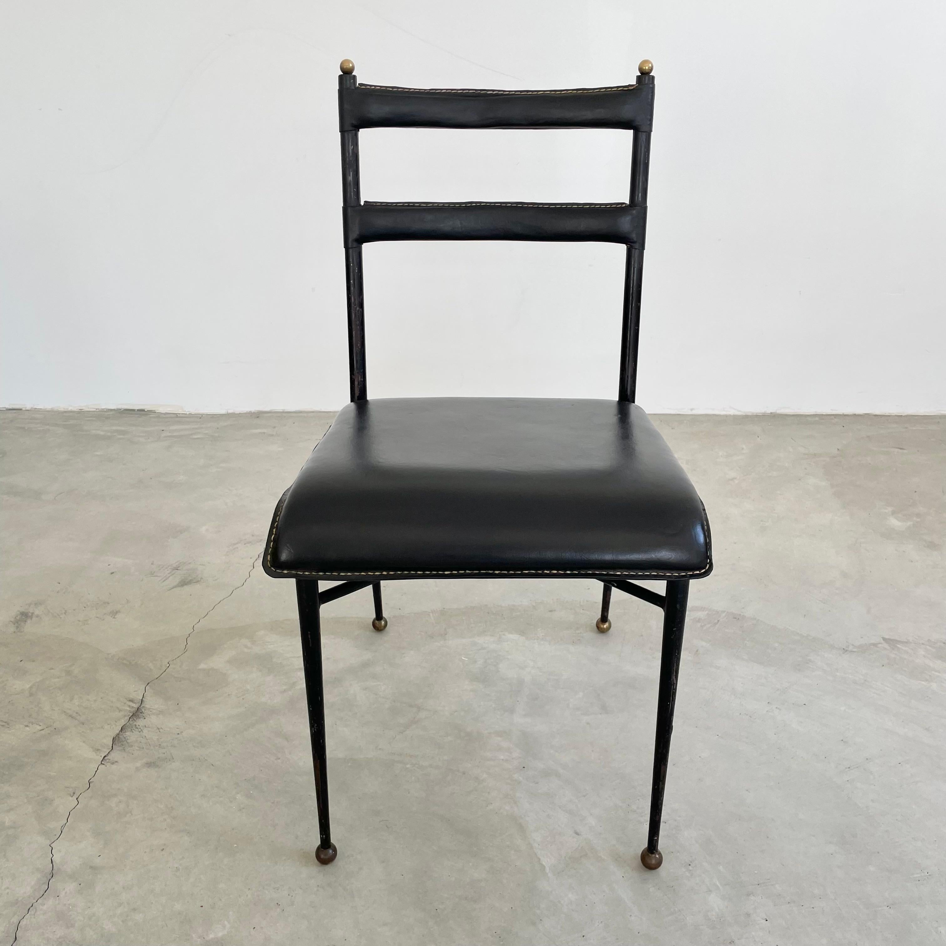 Stunning black leather armchair by French designer Jacques Adnet. Black metal frame with tapered legs, ending in brass ball feet. Brass balls adorn the top of the frame as well. Thick leather seat and backrests hand-stitched in the characteristic