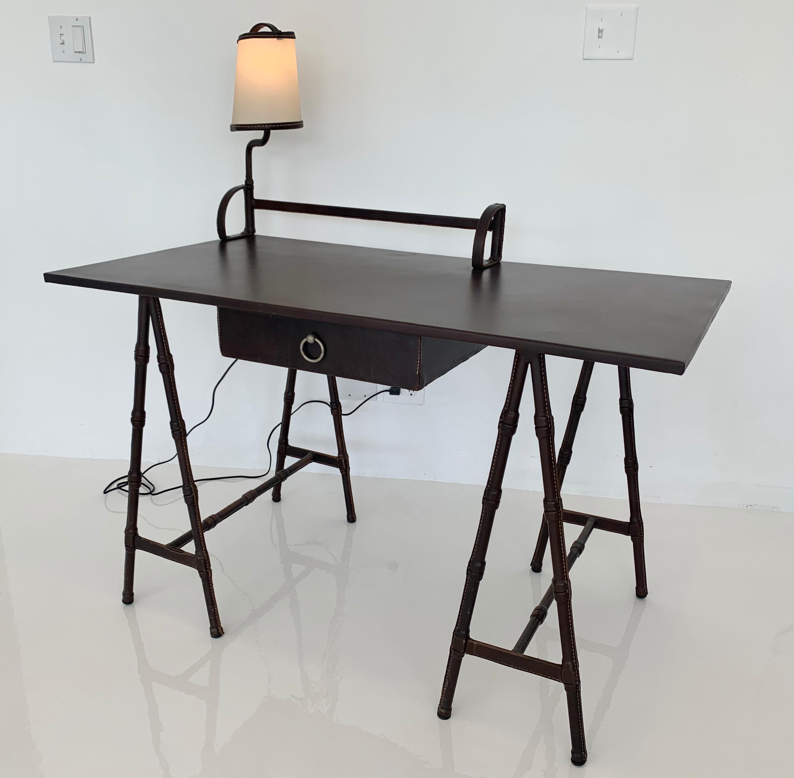 Monumental leather desk by French designer Jacques Adnet. Built in bookshelf. Built in swivel lamp. Newly rewired. Entire desk and all parts completely wrapped in chocolate brown leather. Signature Adnet contrast stitching. Pull out drawer with