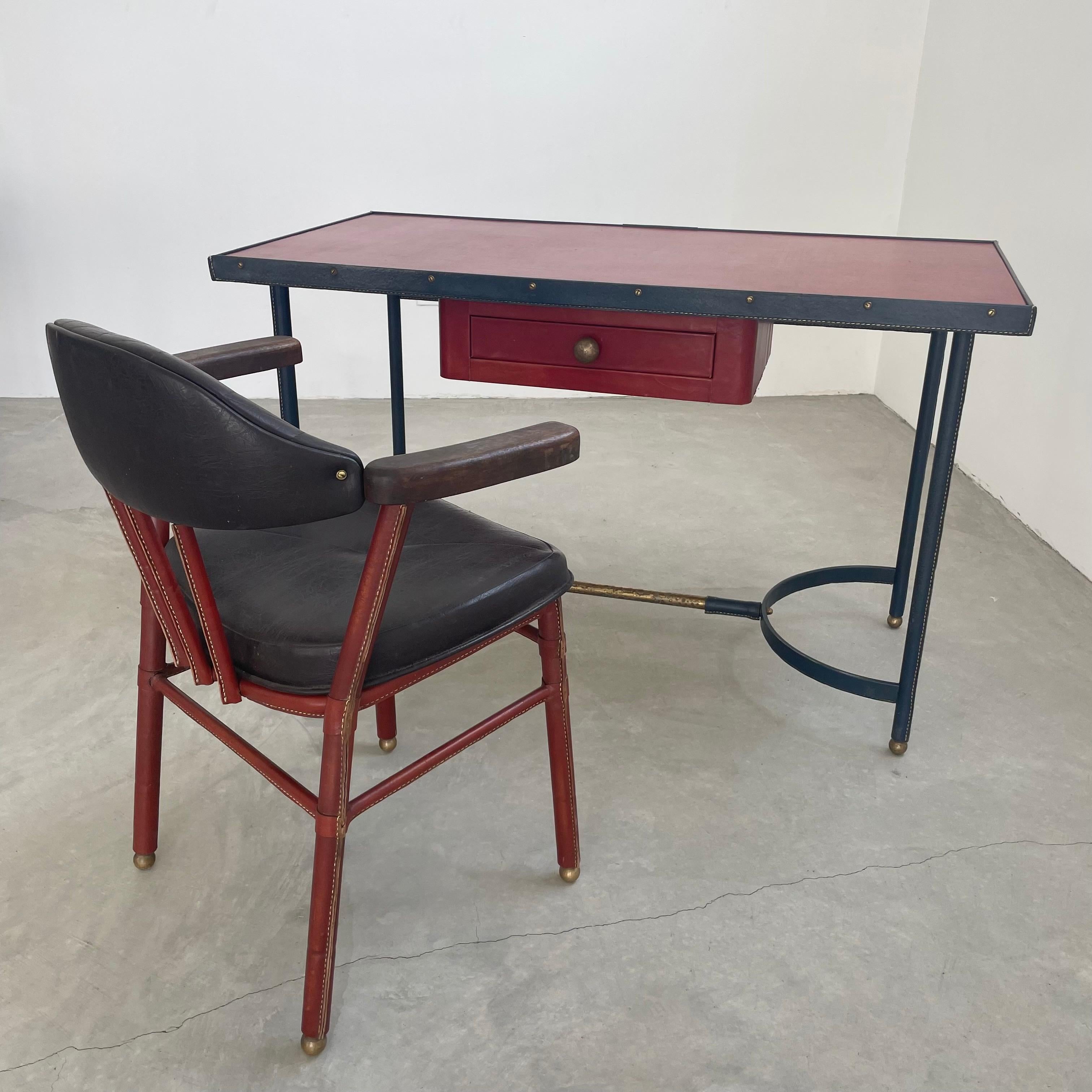 Exceptional Art Deco era desk with matching chair by French modernist designer Jacques Adnet. Entire desk is wrapped in leather. Iron frame with 4 posts, inverted u-shaped bases and brass support bar/foot rest connecting the two. Heavy iron frame