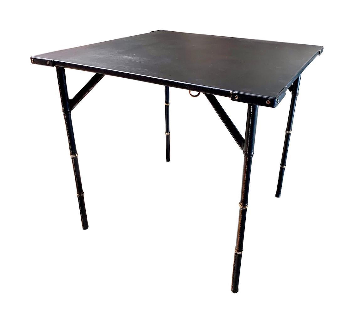 Stunning leather table by French designer Jacques Adnet. Leather wrapped bamboo style legs with leather wrapped top and corners. Brass detailing throughout. Signature Adnet contrast stitching throughout. Excellent vintage condition. Game table folds