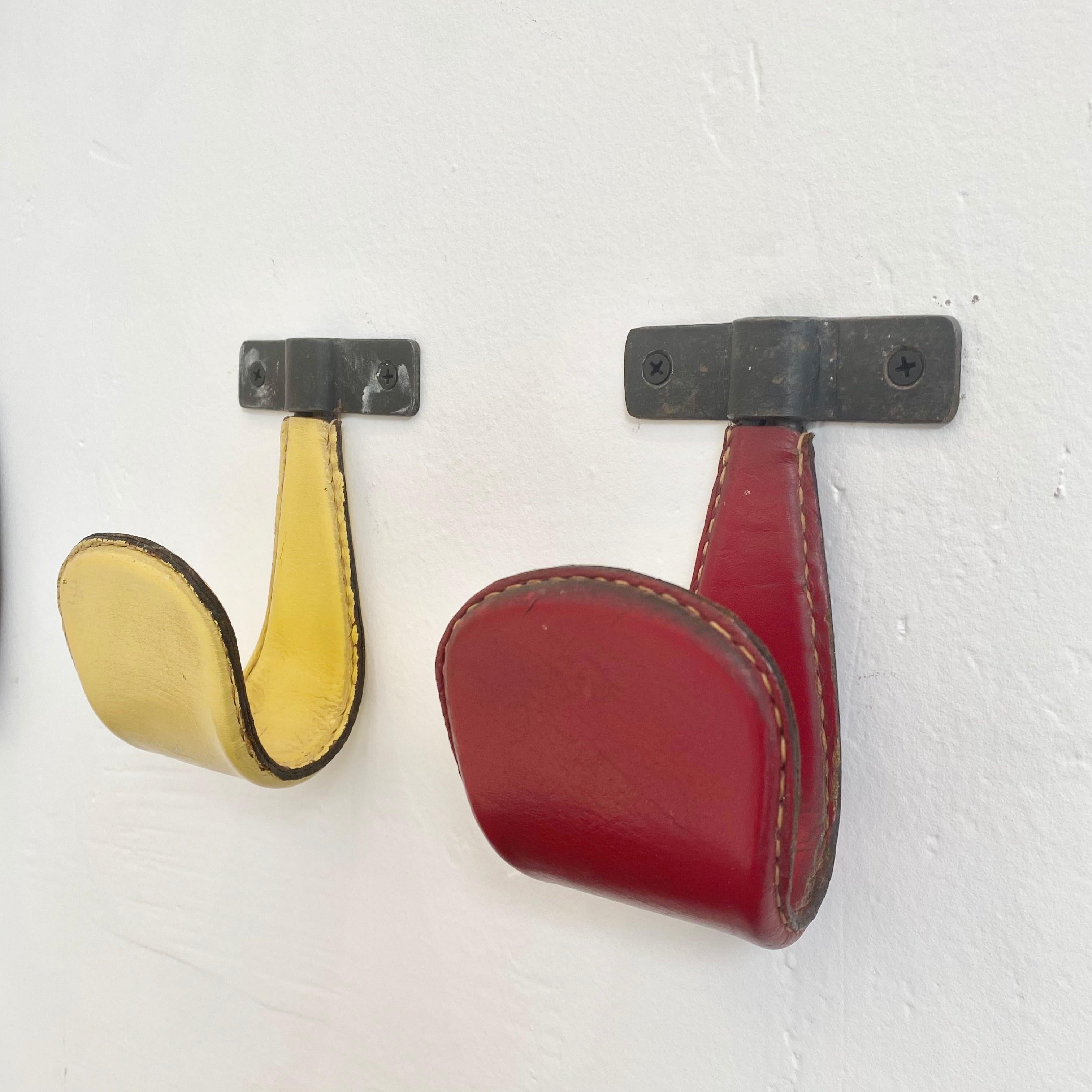 Vintage leather and iron tongue hooks by French designer Jacques Adnet. One red hook and one yellow hook. Good vintage condition. Priced individually.