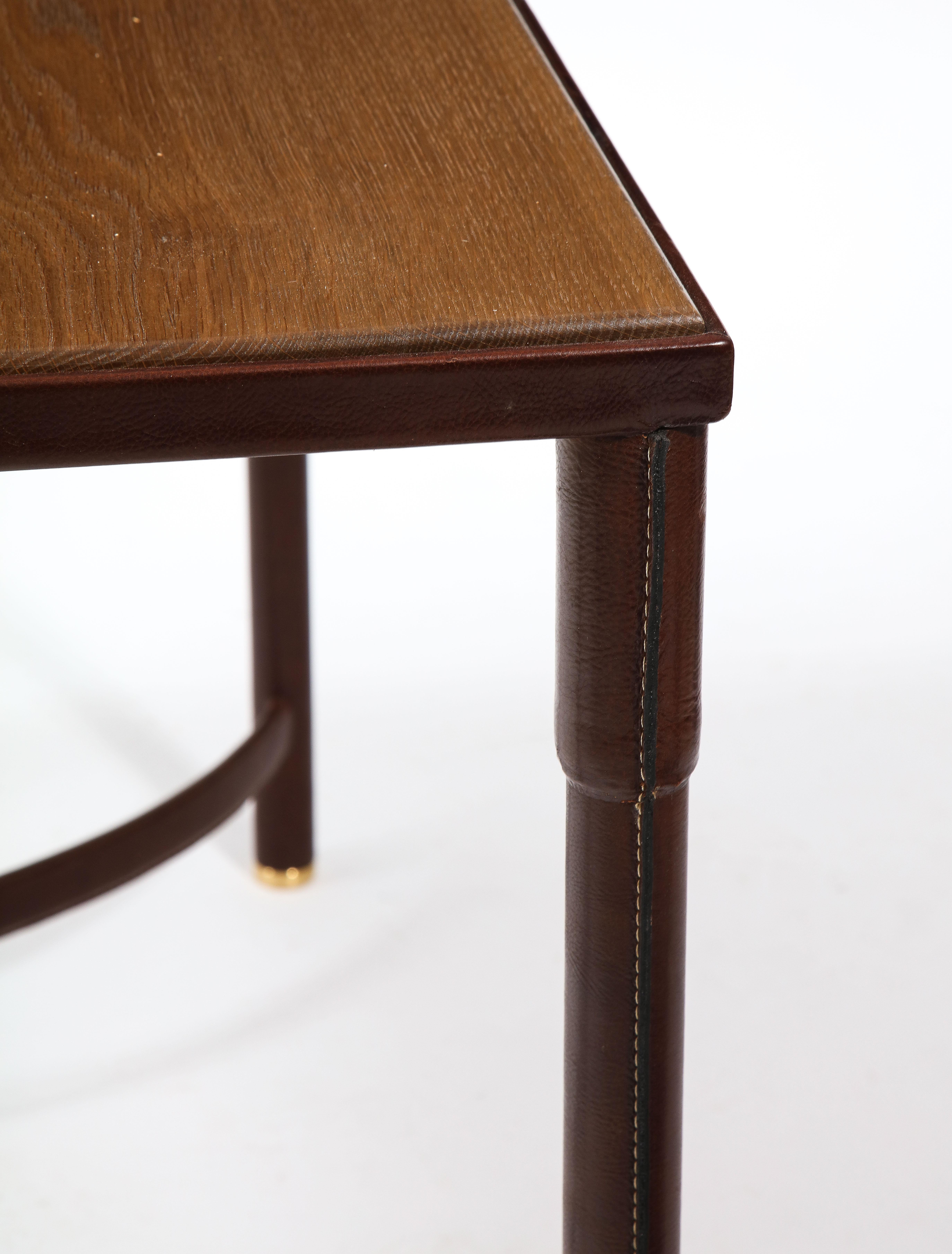 Elegant Jacques Adnet center table or writing desk in stitched leather with an oak top. The leather was expertly restored as per the original by the foremost restoration studio in the USA. It has a double-sided U-shaped stretcher connected by a