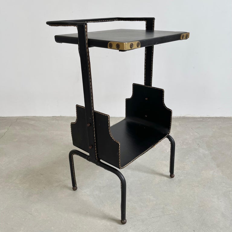 Stunning leather telephone/side table by Jacques Adnet. Iron frame completely wrapped in black leather with tabletop and lower shelf. Signature Adnet contrast stitching. Brass ball feet and brass corners. Great vintage condition. Super functional