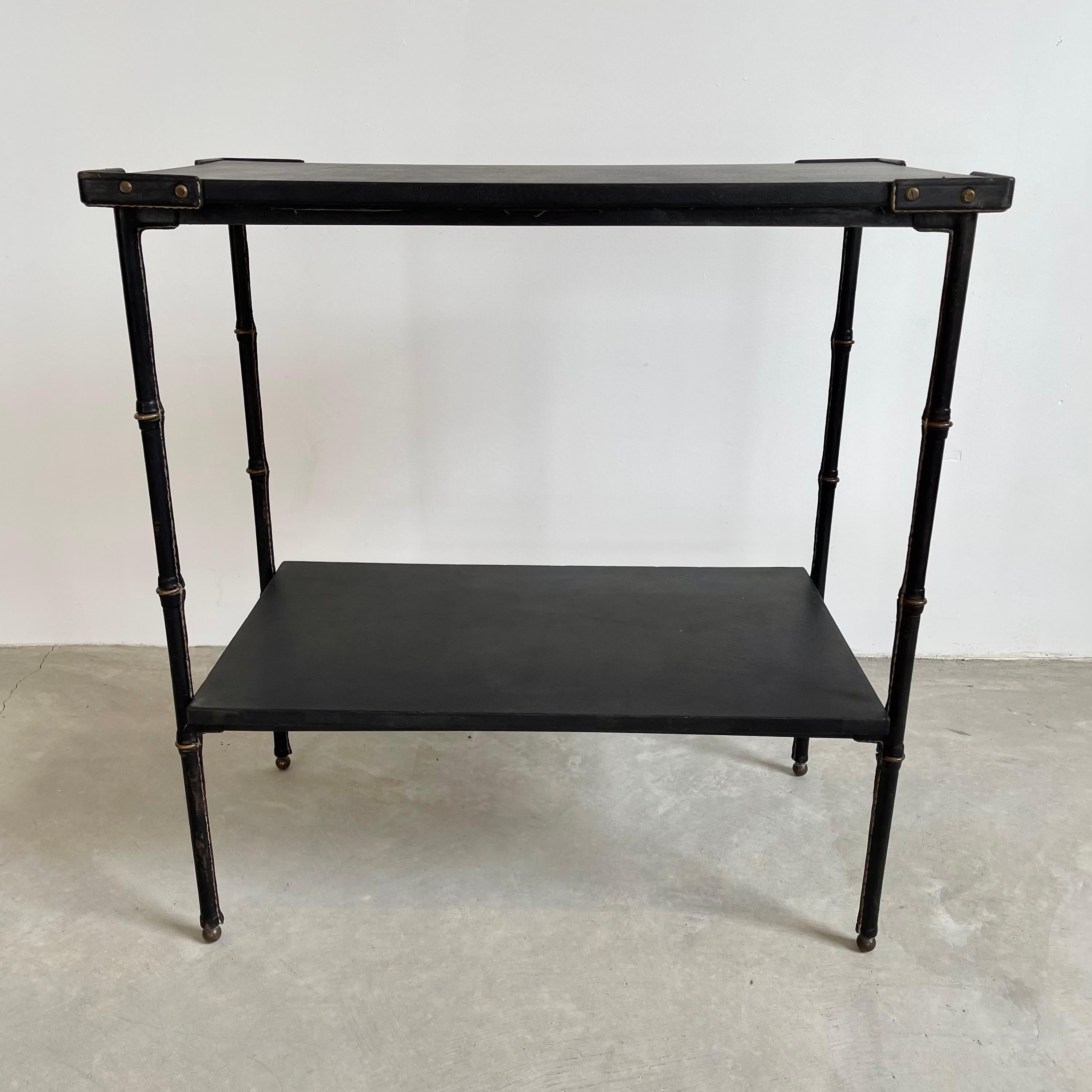 Large leather side table by French designer Jacques Adnet. Entirely wrapped in black saddle leather. Leather wrapped legs with brass detailing, and brass ball feet. Second leather shelf underneath making this piece great for storage. Tabletop edges