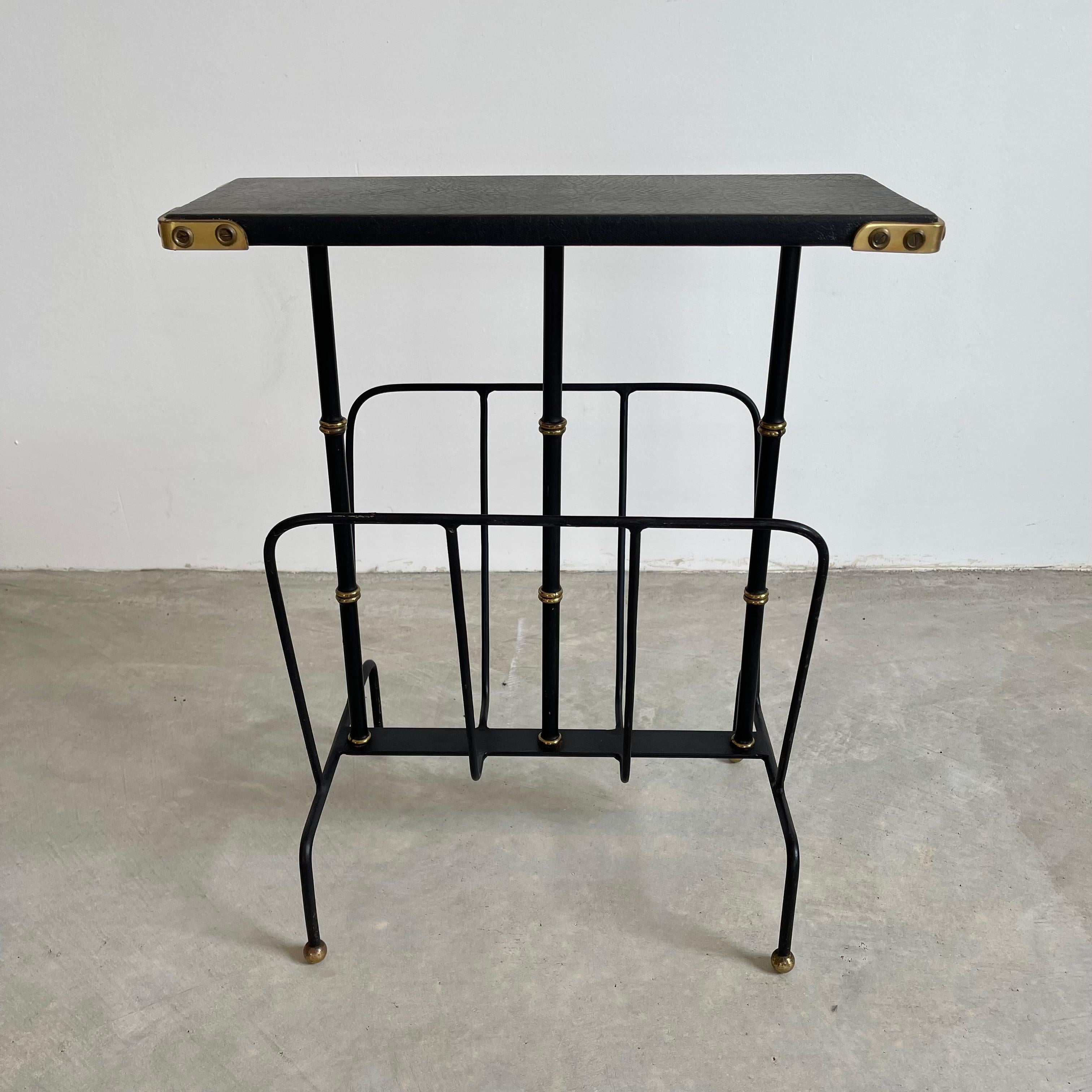Fantastic leather side table by French designer Jacques Adnet. Leather wrapped legs with brass detailing, and brass ball feet. Metal rack underneath the slender leather table top for storing books or magazines. Edge of tabletop is wrapped in black