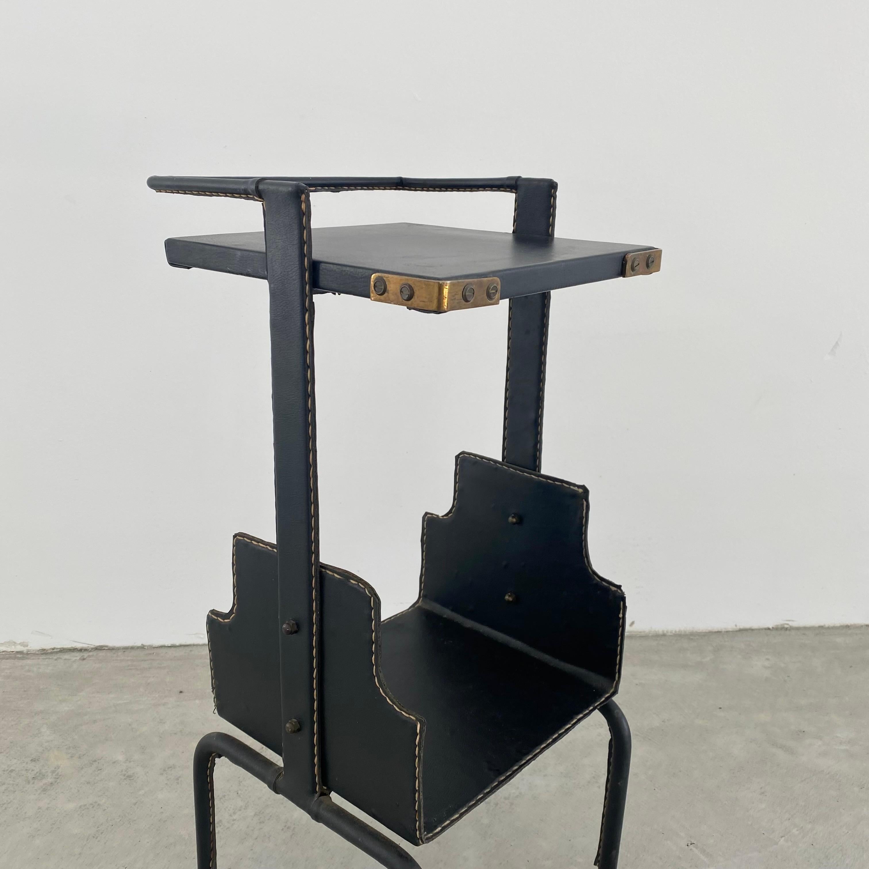 Stunning leather side table by Jacques Adnet. Completely wrapped leather frame with tabletop and lower shelf. Signature Adnet contrast stitching. Brass ball feet and brass corners. Great vintage condition. Super functional piece. Perfect piece of