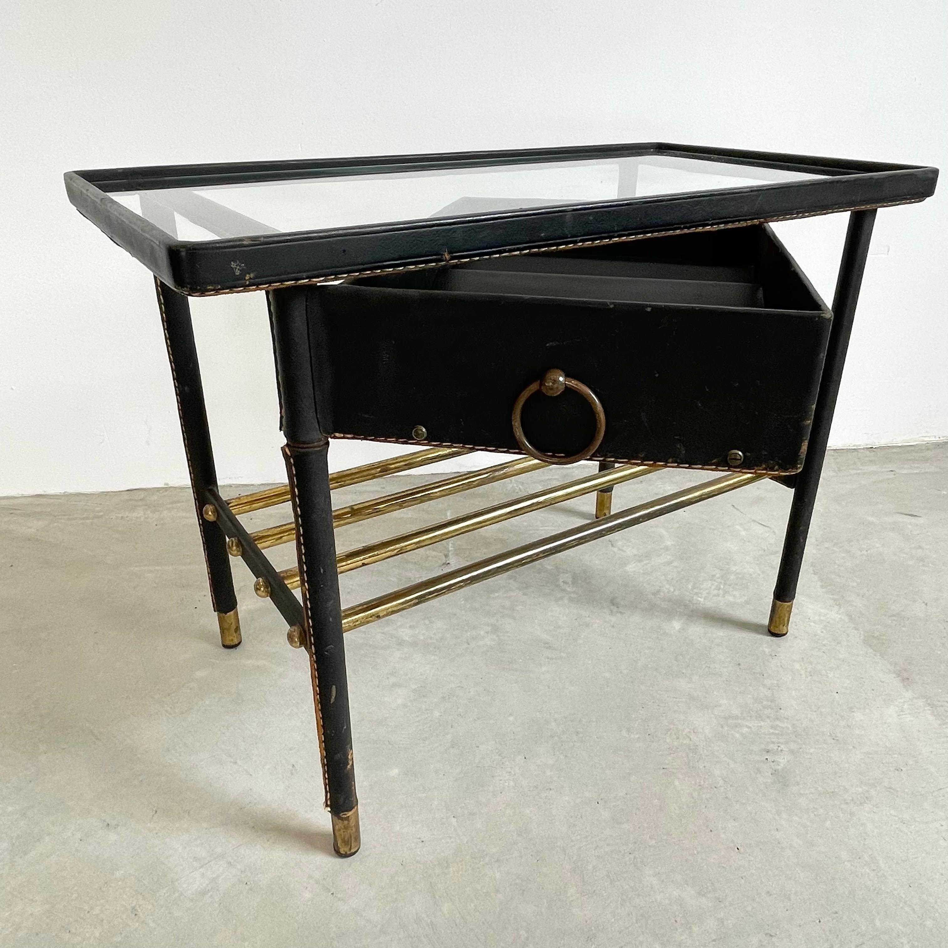 Table d'appoint en cuir Jacques Adnet avec plateau en verre et tiroir pivotant. Toute la table est enveloppée de cuir noir avec des surpiqûres contrastantes signées Adnet. Le tiroir pivote facilement à 180 degrés par rapport à la table, puis se