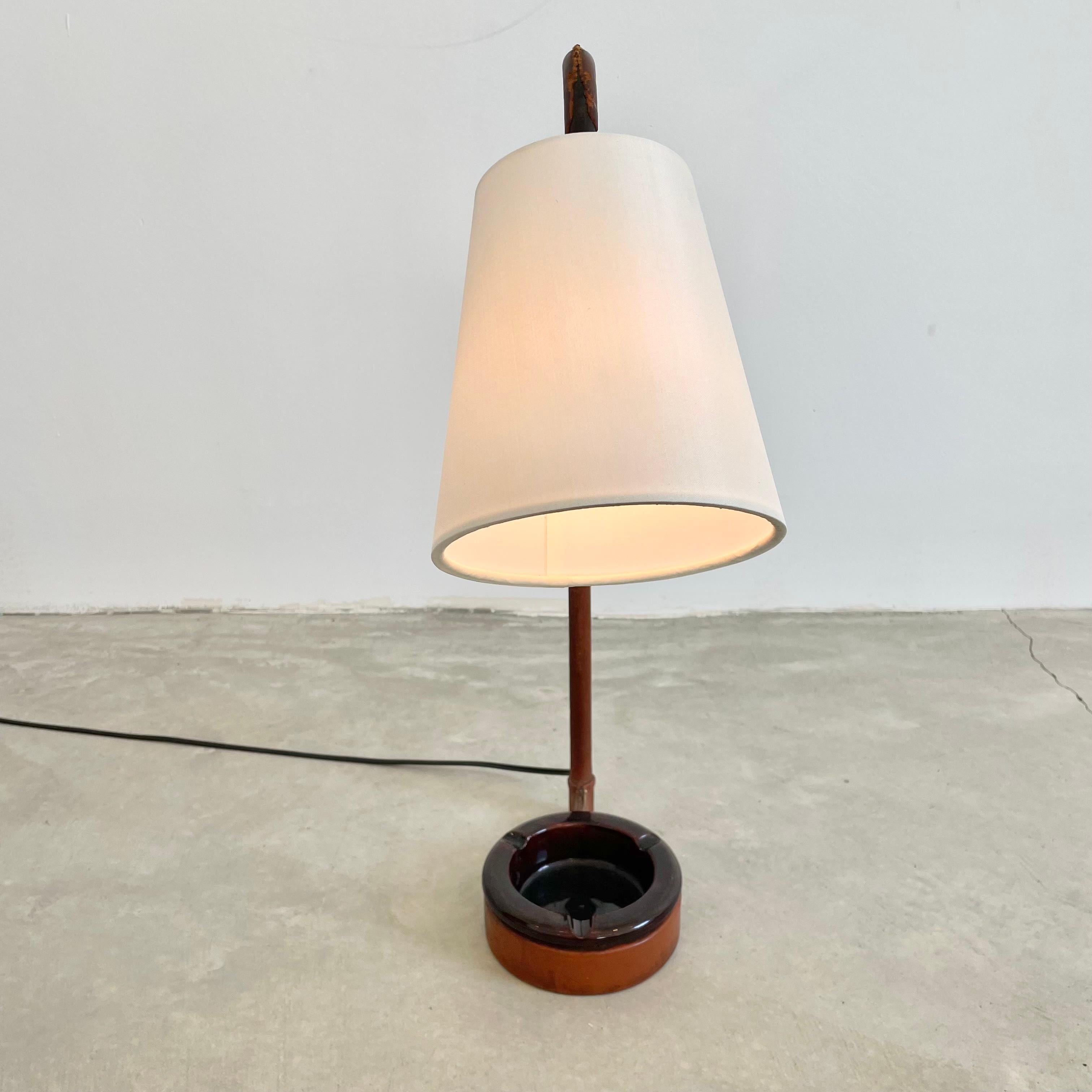 Beautiful Jacques Adnet leather table lamp with brown ceramic ashtray/catchall inset into the base. Metal frame completely wrapped in a tan saddle leather. Lamp is on a ball socket allowing the light to be pointed in different directions. Signature