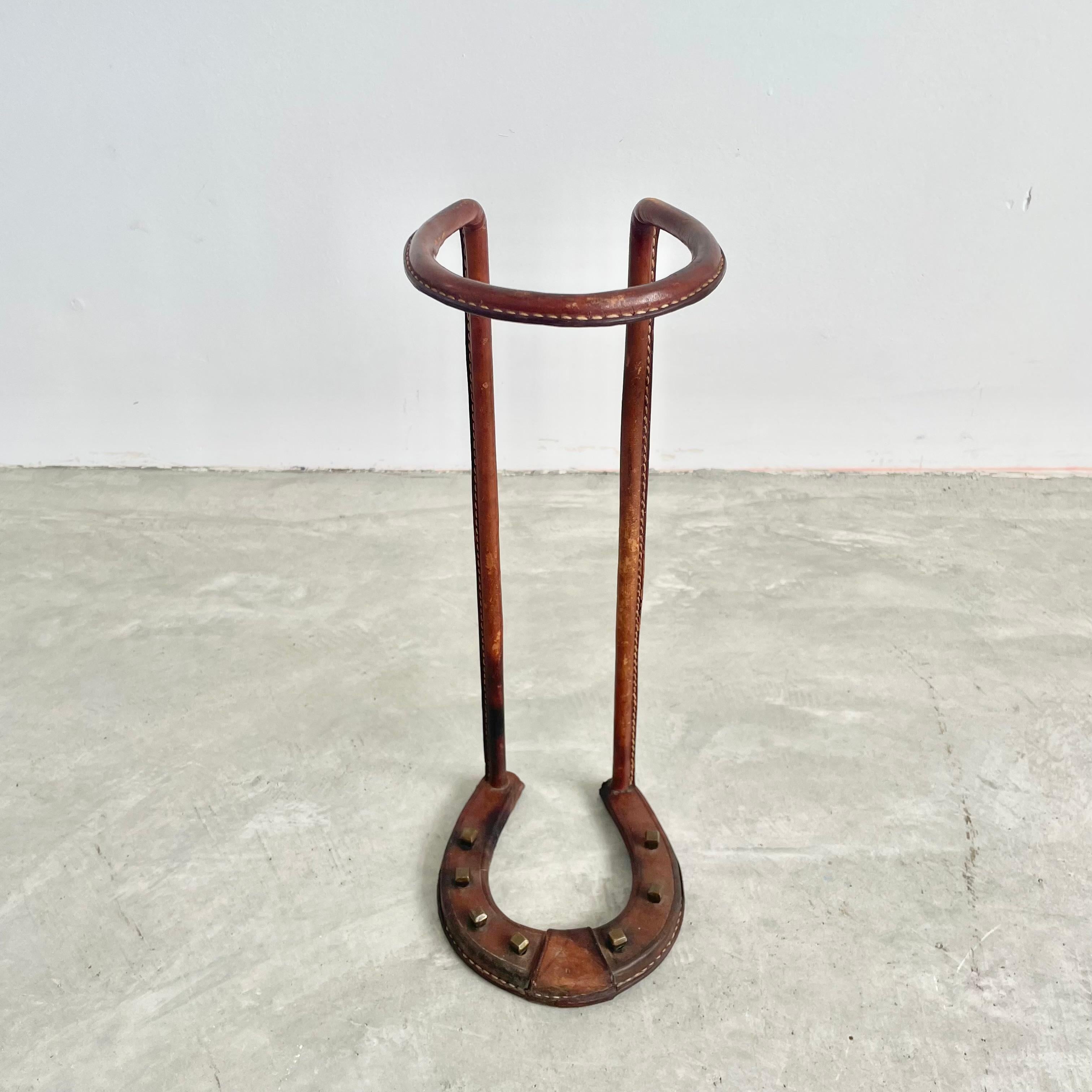 Incredible umbrella stand by Jacques Adnet. Iron frame fully wrapped in saddle leather with all seams stitched together with Adnet's signature contrast stitching. Equestrian motif with the base in the shape of a brass studded horseshoe. The upper