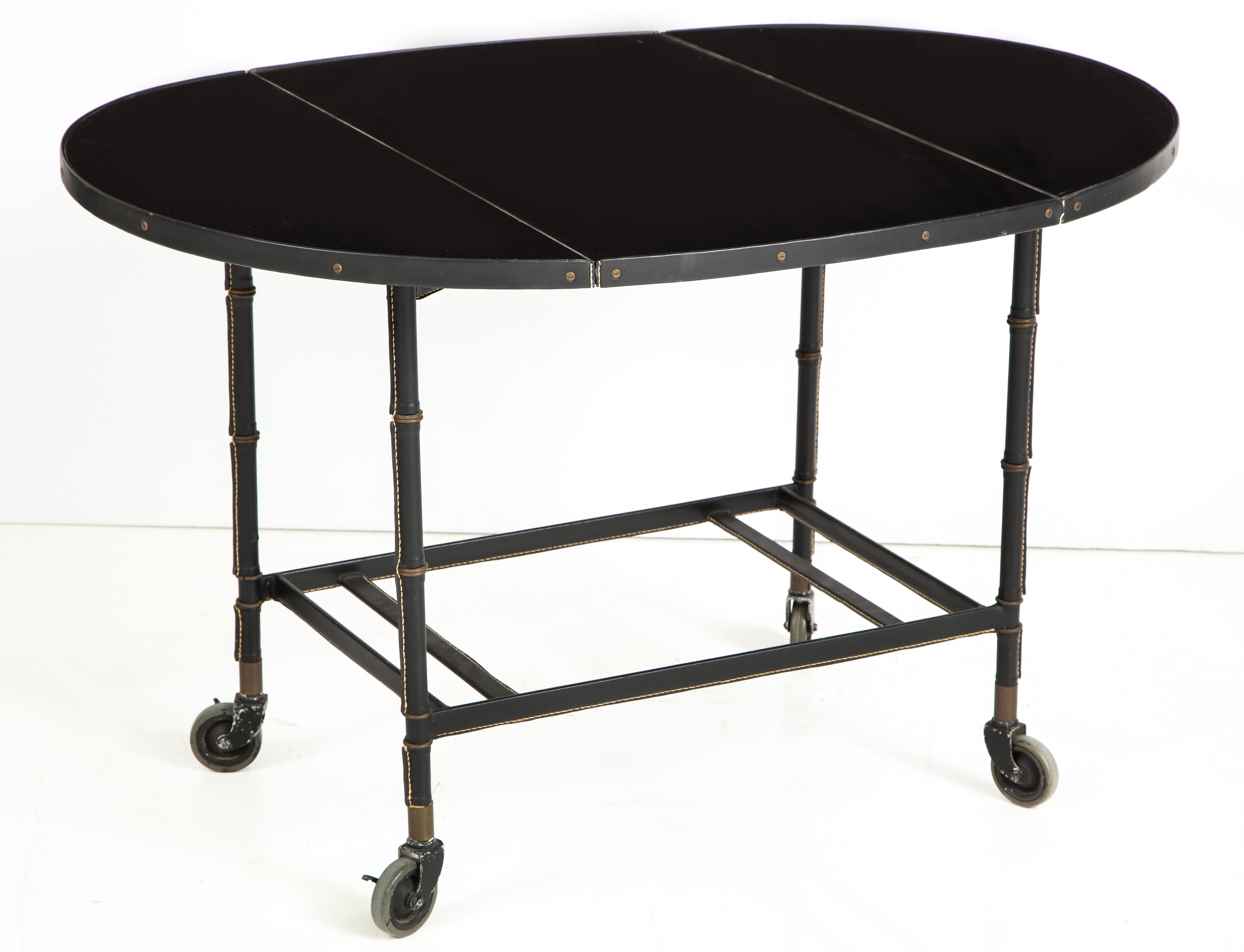 A fine example of Adnet's work with stitched leather covered legs and a black lacquered top. The drop leaf design allows for easy placement and the casters make it a versatile serving table. The indicated measurements are when open. When the leaves