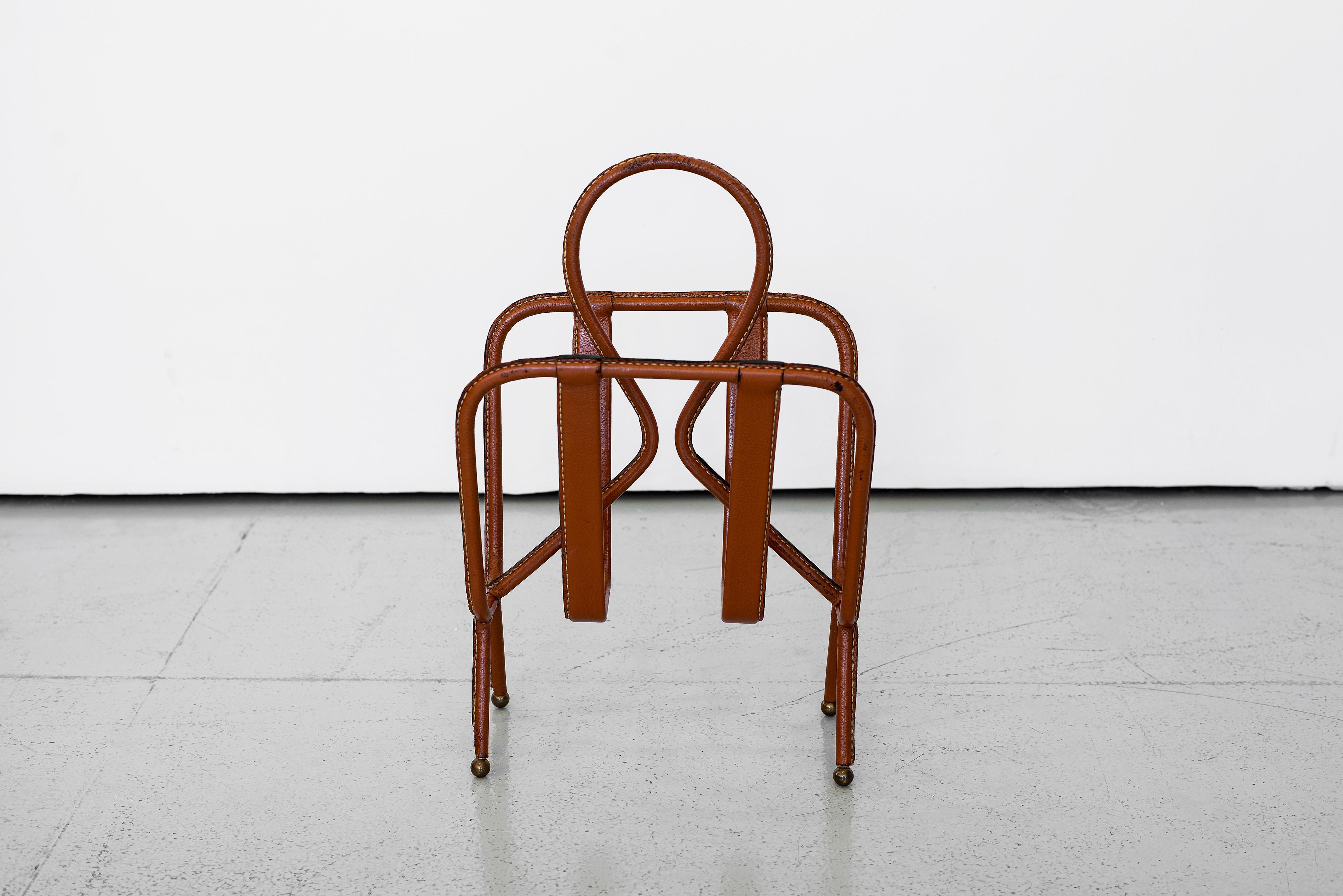 Classic leather magazine rack by Jacques Adnet. Rich brown leather with contrast white stitching and brass ball feet. Very good vintage condition.