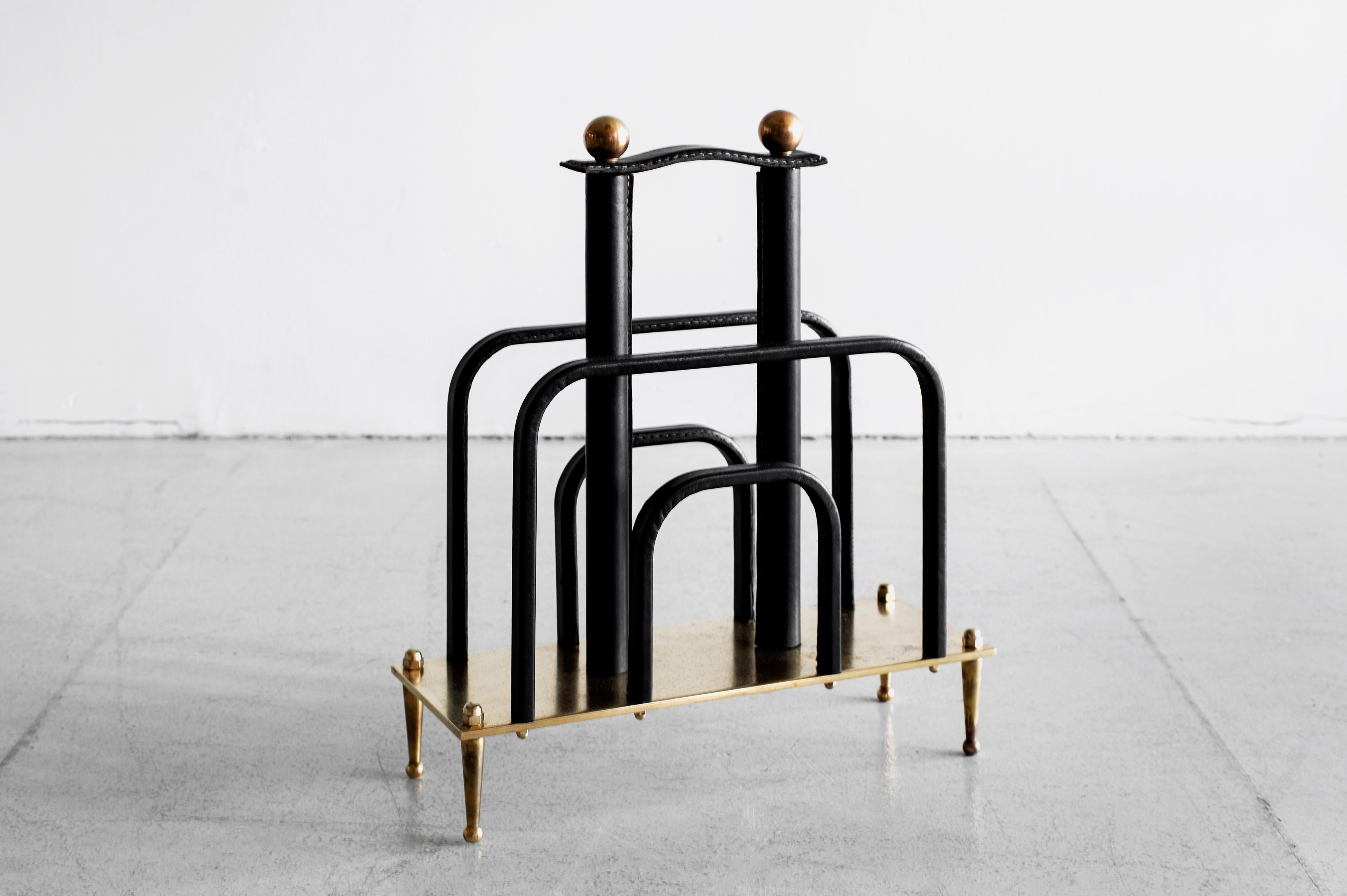 Handsome magazine rack by Jacques Adnet with signature black leather and contrast stitching. 
With brass base and brass ball handles.