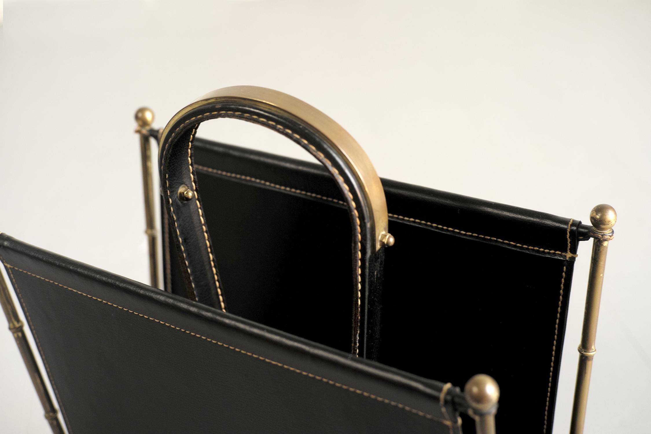 Magazine rack in black leather and brass by Jacques Adnet for the Compagnie des Arts Français, 1950. The structure in gilded brass in a bamboo style is finished with spheres, the sides, the bottom and the large central handle are sheathed in thick