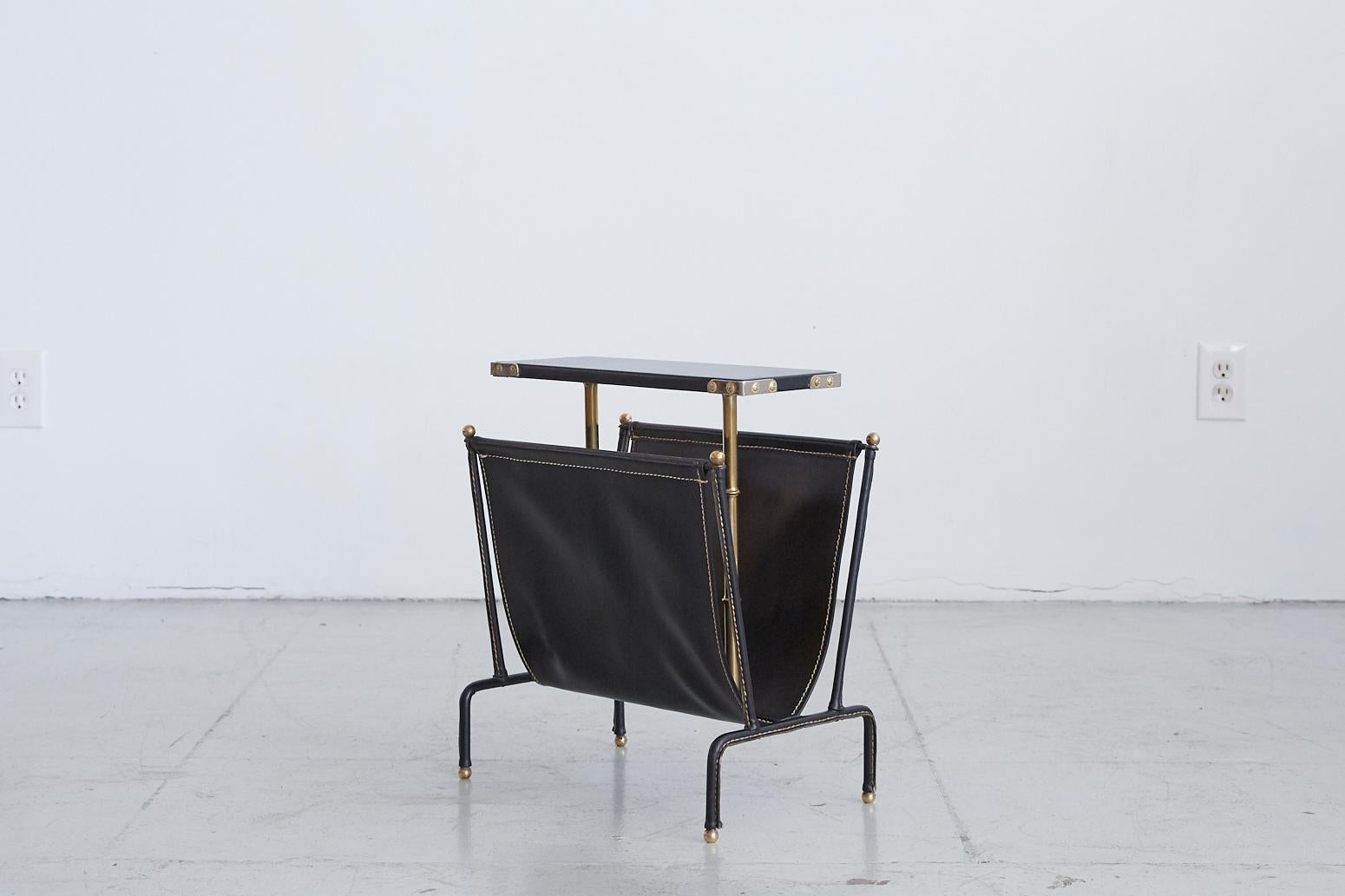 Jacques Adnet table with magazine rack. Black skai tabletop with black leather magazine rack and white contrast stitching. Beautiful brass bamboo leg detailing.