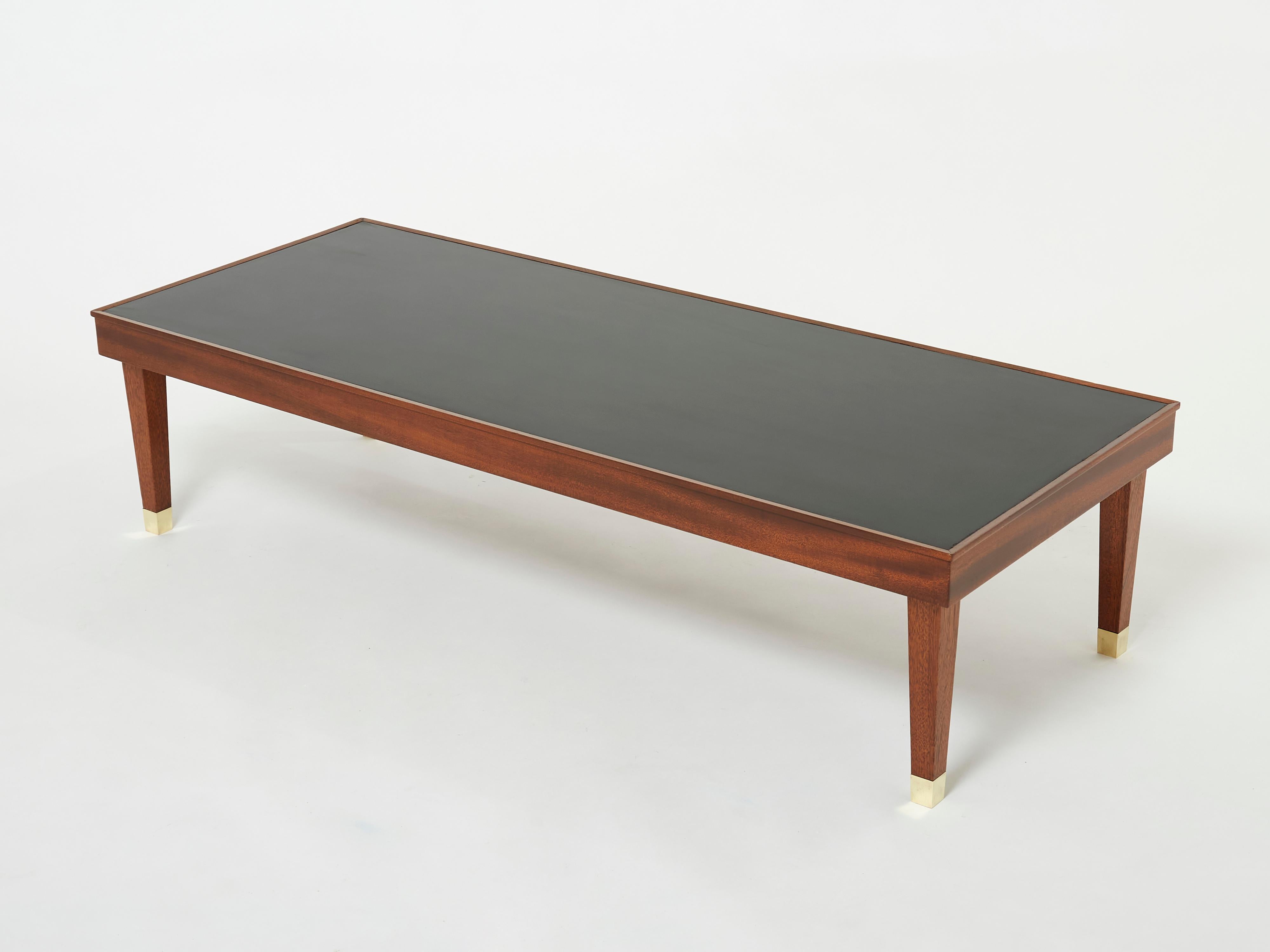 This elegant Jacques Adnet coffee table is sure to add an element of French modernisme to any room in your home. It was designed and produced by Jacques Adnet in the 1950s. With shapely solid mahogany wood structure, tapered legs, brass sabots and a