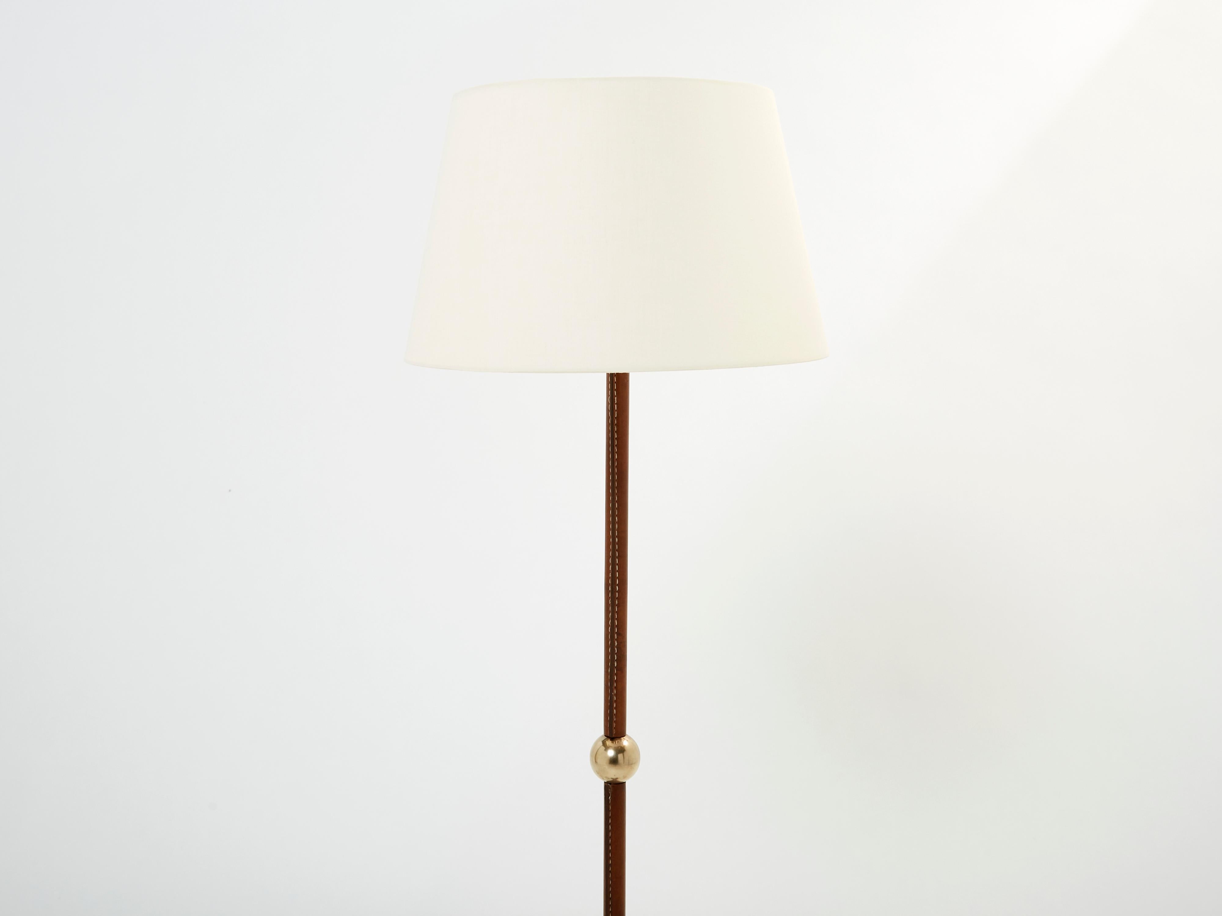 This elegant Jacques Adnet floor lamp is sure to add an element of French modernisme to any room in your home. It was designed and produced by Jacques Adnet in the 1950s. With piqué sellier stitched brown leather structure, with brass accents, brass
