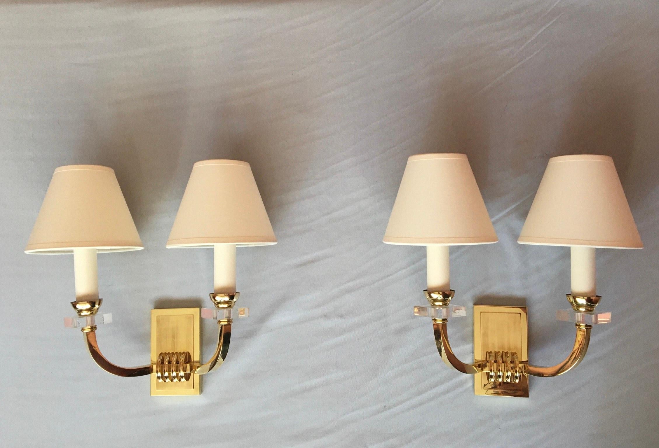 Very elegant pair of gilded bronze, brass and plexiglass double arm wall sconces in the French neoclassical style of the 1950s by Jacques Adnet. 
The sconces are in a really very good good condition, new rewired and fit the US standards. They come