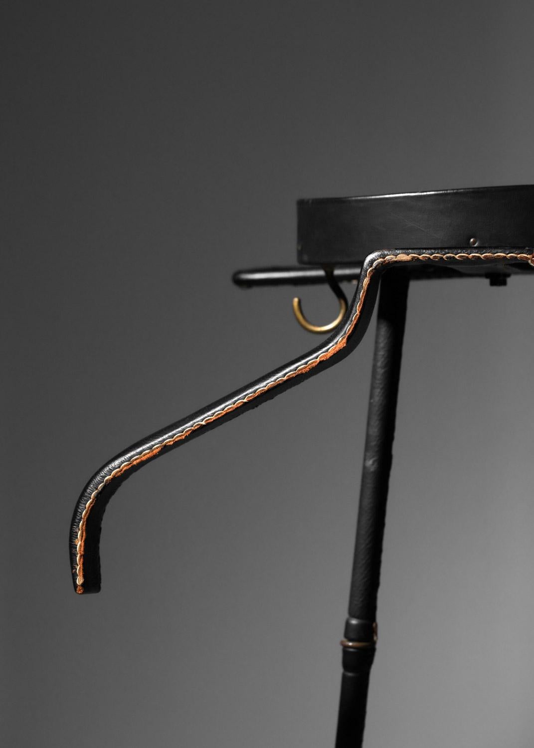 50's night valet by French designer Jacques Adnet. Wooden and lacquered metal structure covered in sheathed black leather (original leather), embellished with two solid brass coat hooks. Very fine vintage condition, with traces of use and age.