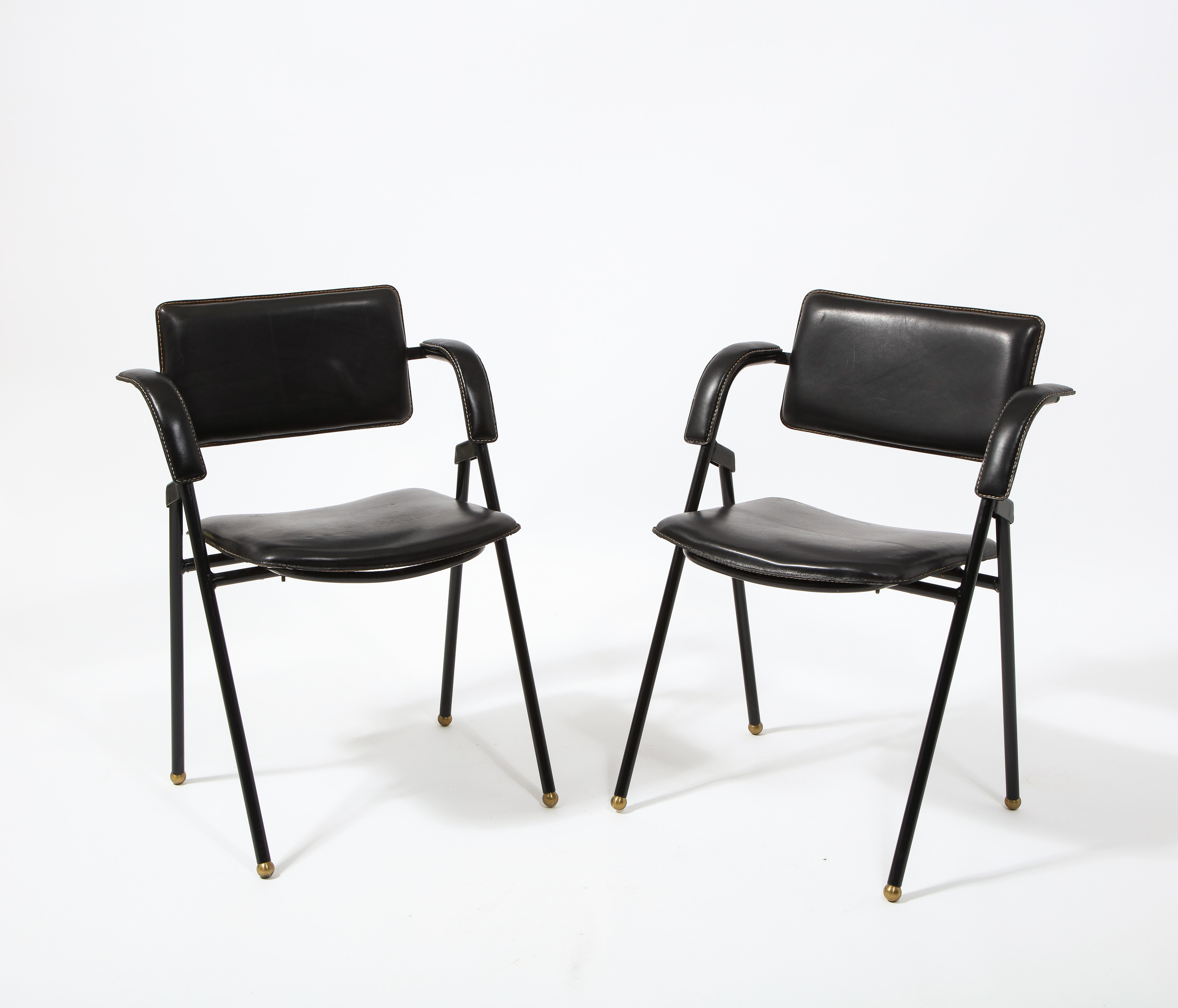 A pair of Jacques Adnet folding chairs in stitched black leather and black enameled frames on brass feet.