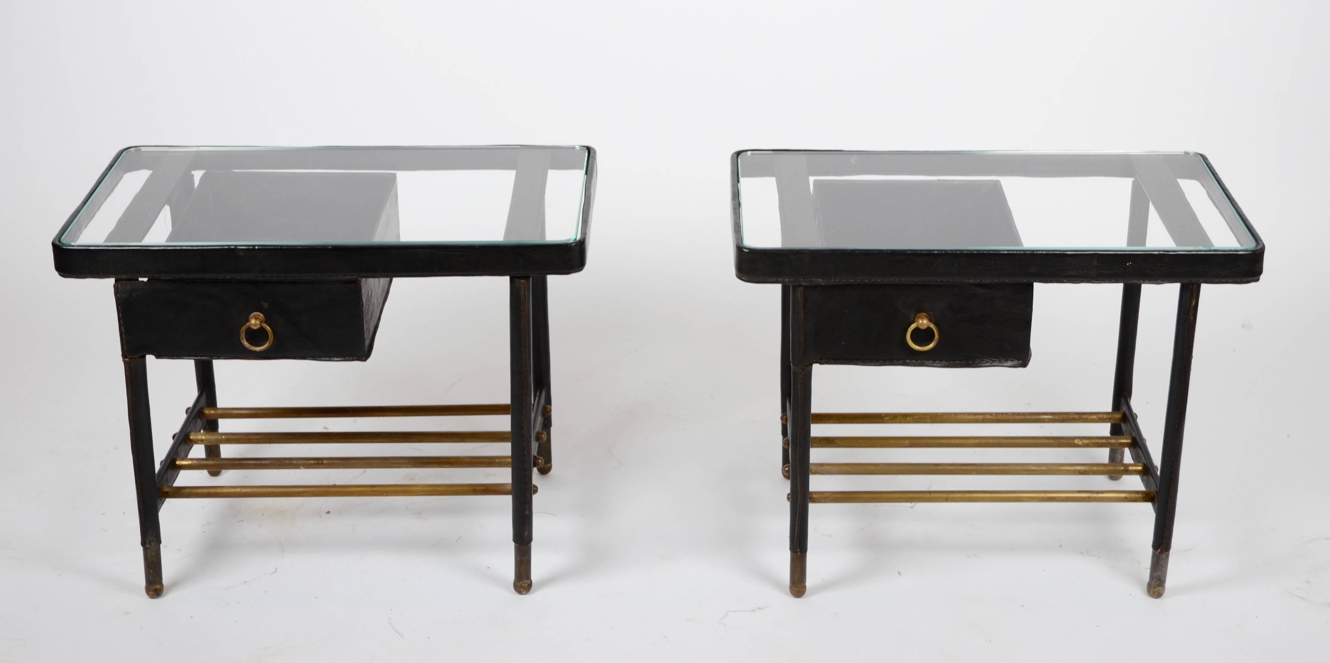 A pair of side tables with drawers, designed by Jacques Adnet, 1950s. Made in leather-bound tubular metal, glass and brass.