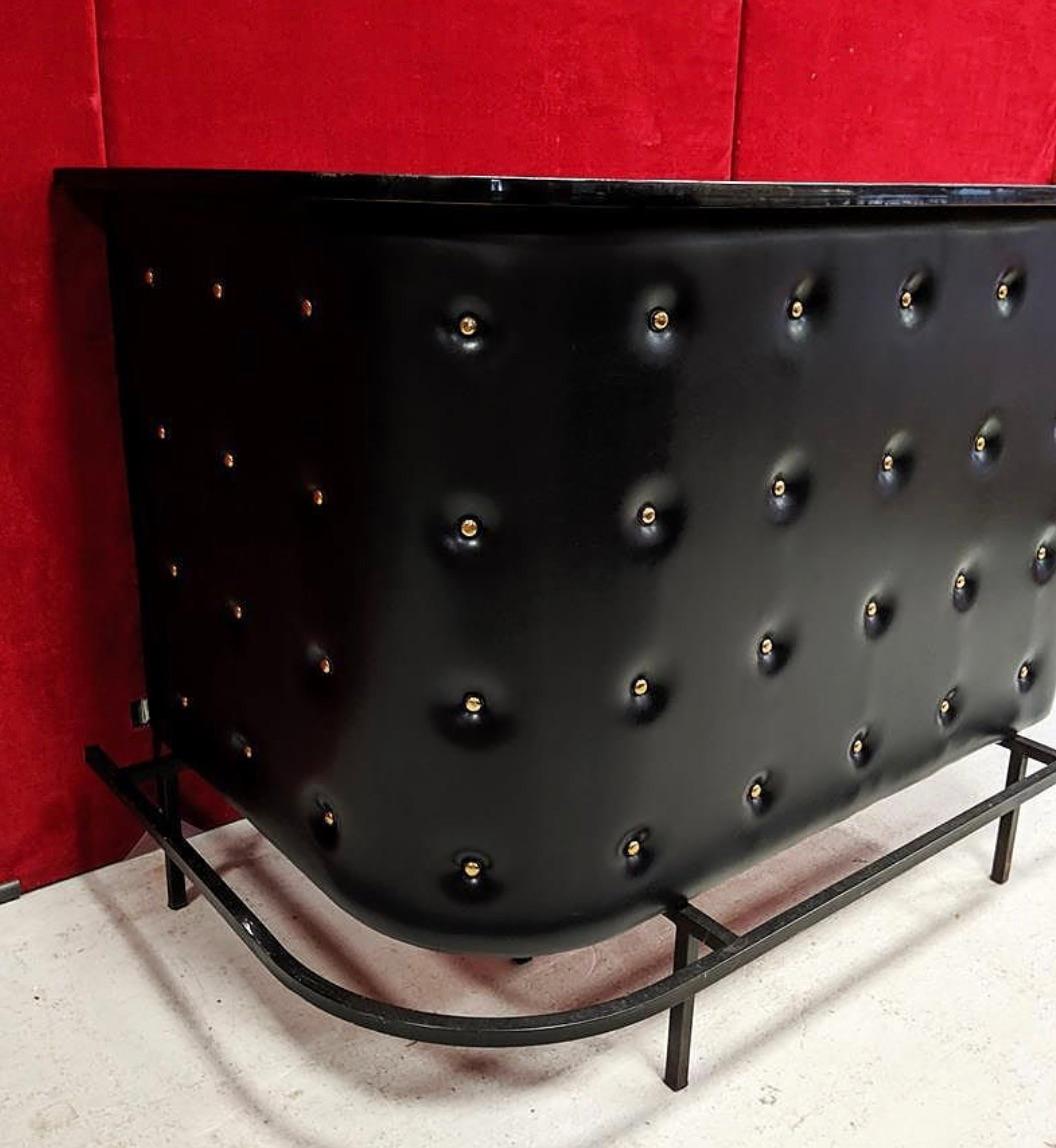 Jacques Adnet. Rare apartment bar wrapped in black leather and brass studs, circa 1950. Measures: Height 100cm., length 120cm., back 86cm. Black lacquered base with footrest on the visitor side. The interior of the bar is equipped with metal shelves