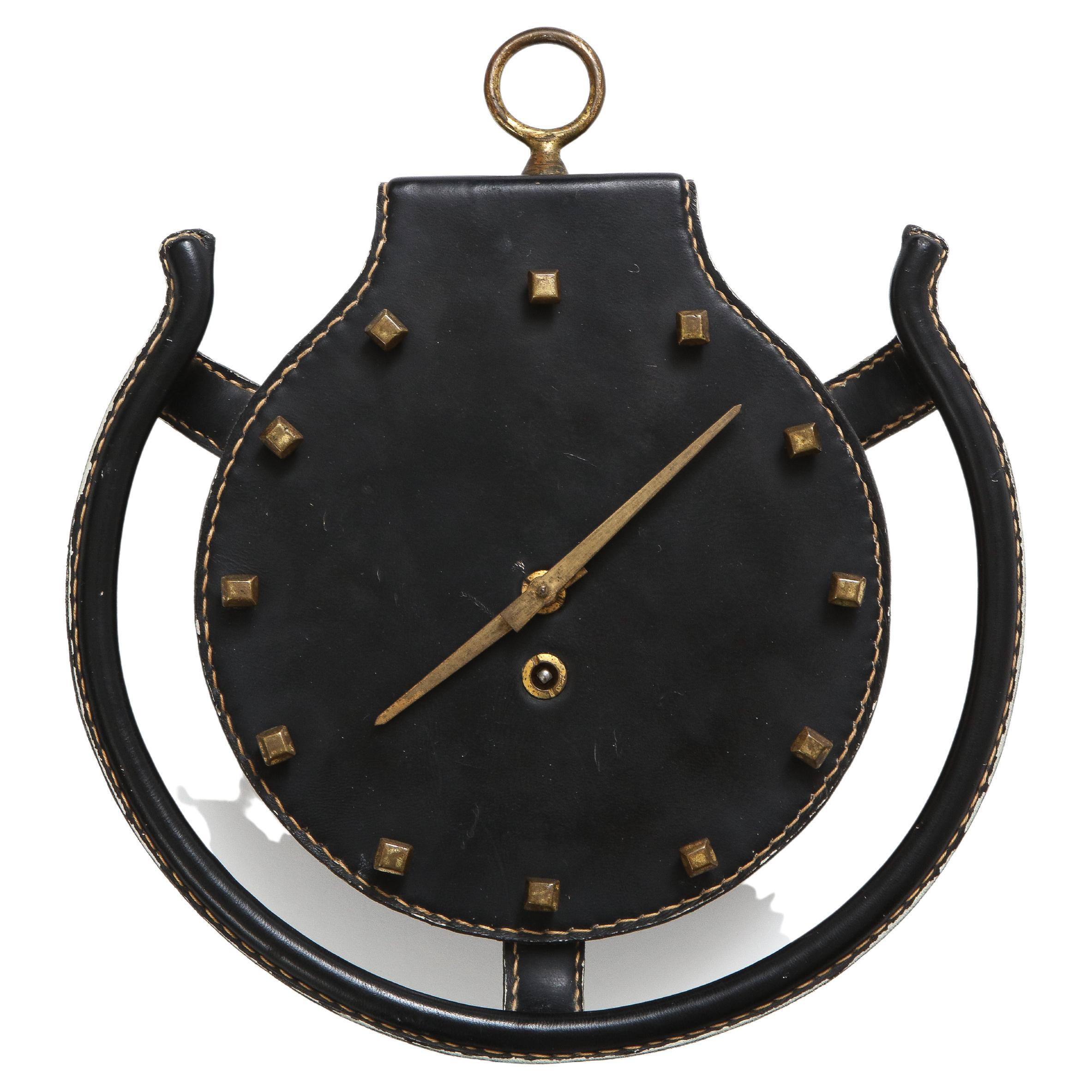 Jacques Adnet rare horseshoe wall clock covered in original black saddle-stiched leather suspended by brass hanging ring with hands and numbers in bronze which evoke farrier nails. Comes with wind up key. Restored and in working order.