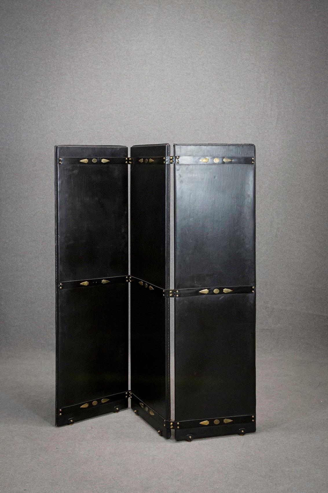 Rare screen designed by designer Jacques Adnet made in 1950. The screen has three mobile doors in black leather. Each door is mobile thanks to its brass and leather hinges. The particularity of the screen is its handmade workmanship. It denotes the