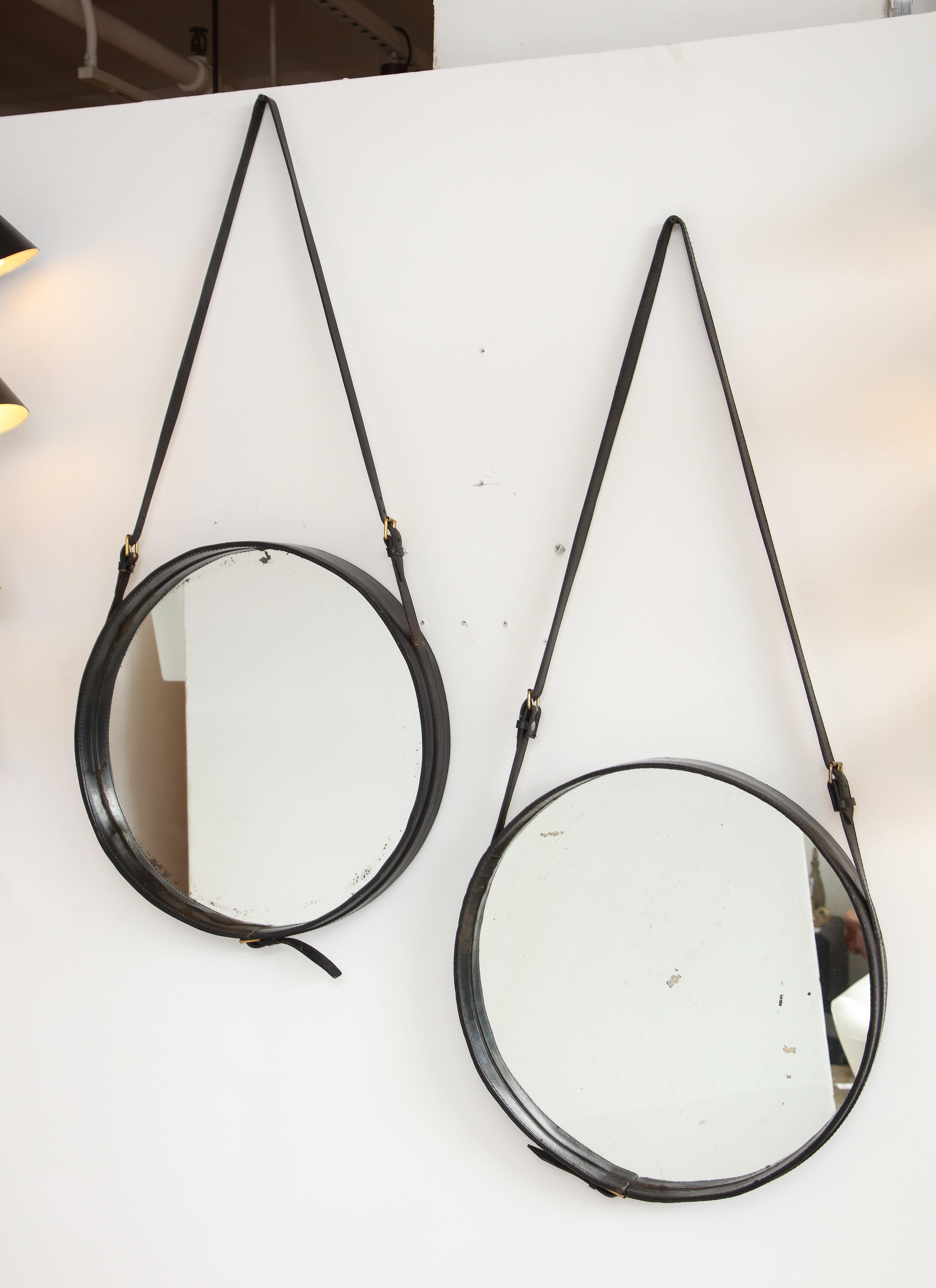 Jacques Adnet, rare paire de miroirs muraux ronds habillés de cuir noir avec des sangles réglables et des verres miroirs d'origine, France, années 1950. Ces miroirs sont restés dans leur état d'origine et en très bon état, sans dommages ou