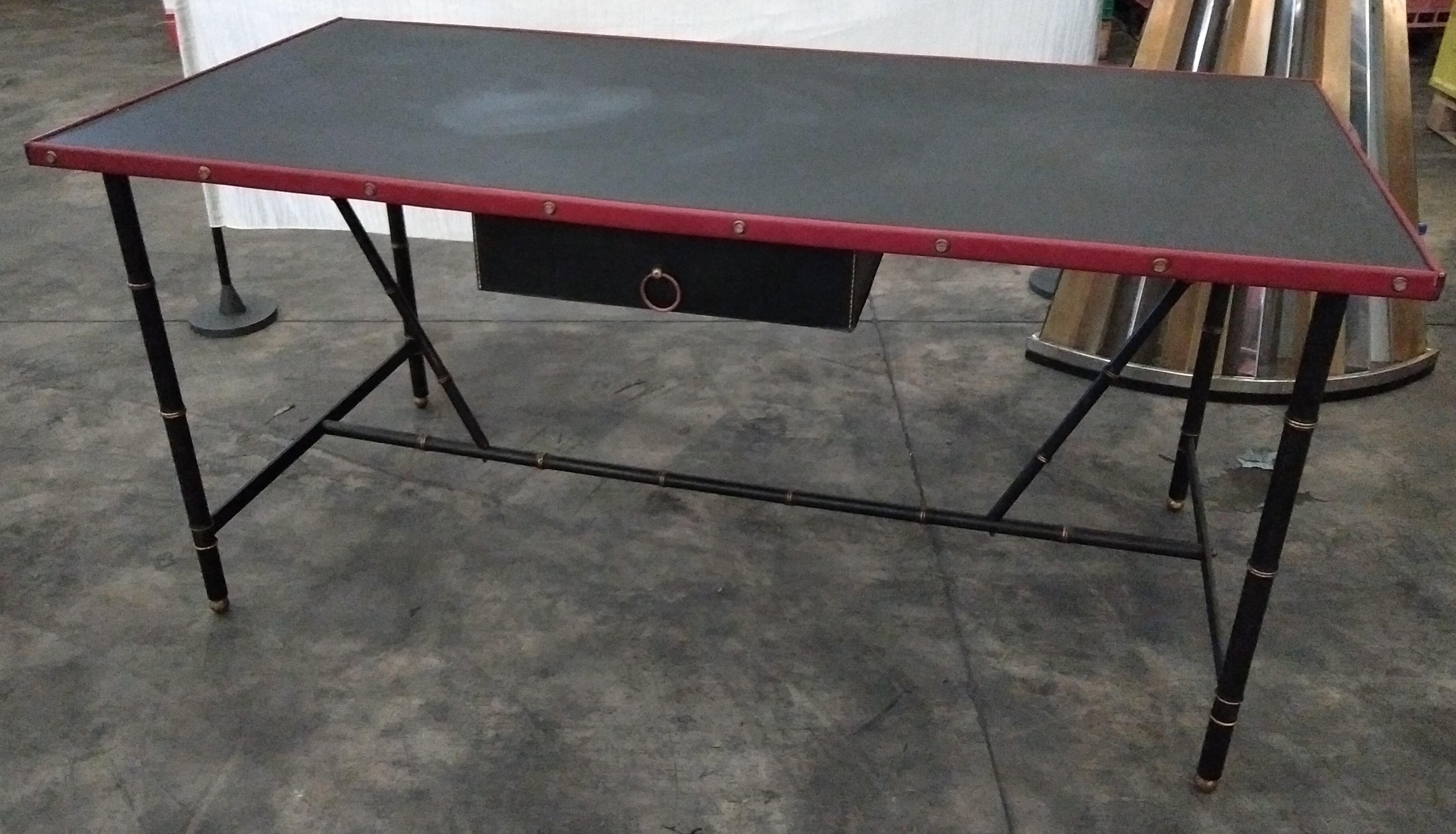 A large red and black desk designed by Jacques Adnet in France in 1950s.
A rectangular tray covered with black leather is framed by uprights wrapped in red leather and brass screws. The oak drawer is also leather wrapped and has a brass
ring
