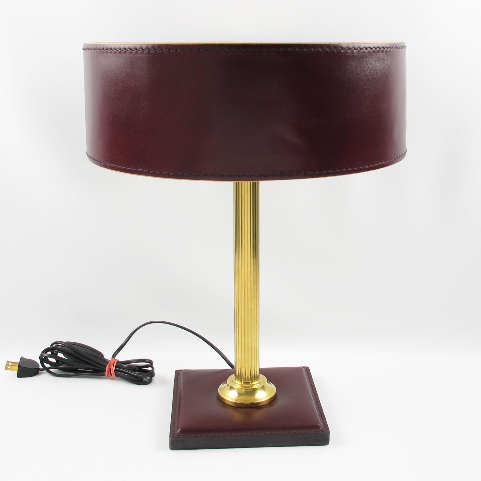 Elegant table lamp designed by Jacques Adnet, France. This stunning classical bordeaux-red color lamp features a hand-stitched shade with ivory paper lining, polished brass reeded column stem, and square base in same hand-stitched bordeaux leather.