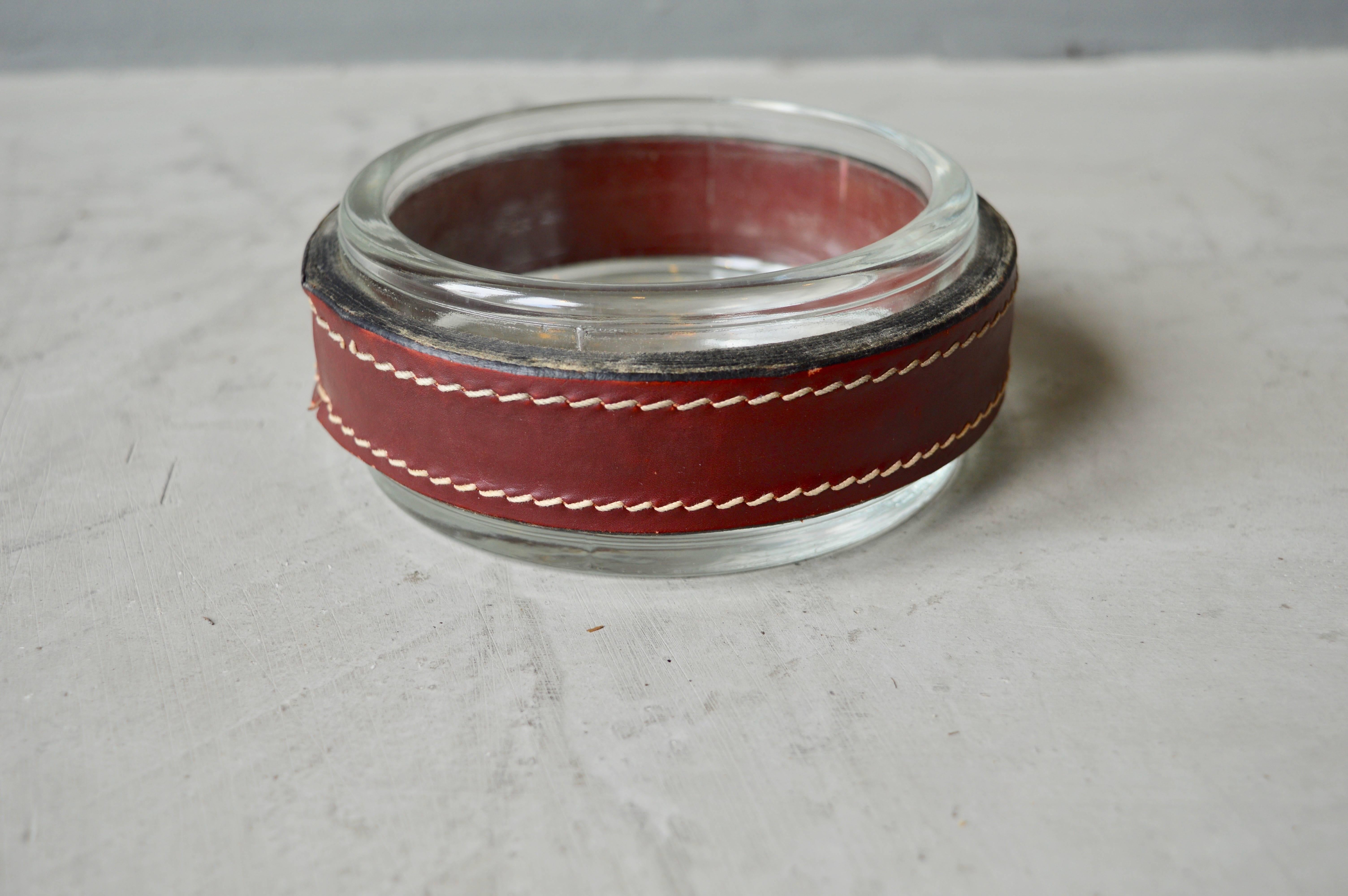 Handsome red leather and glass ashtray or catchall by French designer Jacques Adnet. Signature Adnet contrast stitching throughout. Great desktop piece or catchall to put by the front door. Excellent vintage condition.