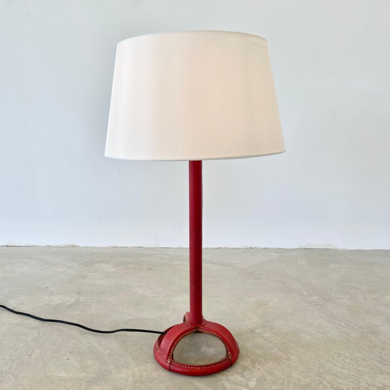 Very rare Jacques Adnet red leather table lamp. Metal frame completely wrapped in a rich red leather. Signature Adnet contrast stitching throughout. Illuminates beautifully. Circular base attached to the stem by three leather wrapped metal arms.