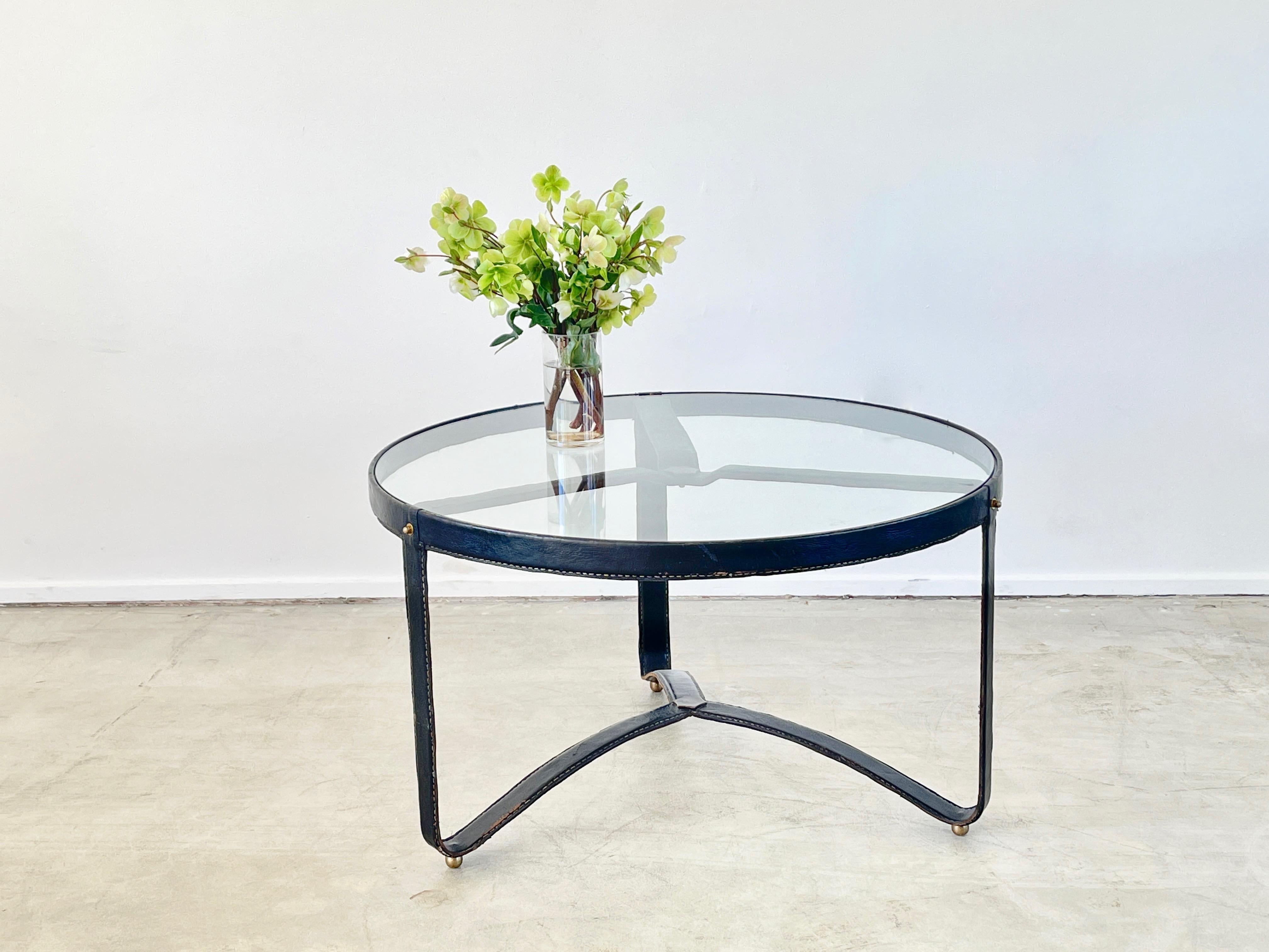 Jacques Adnet round coffee table with signature leather stitching, curved base and brass detailing
New glass top.